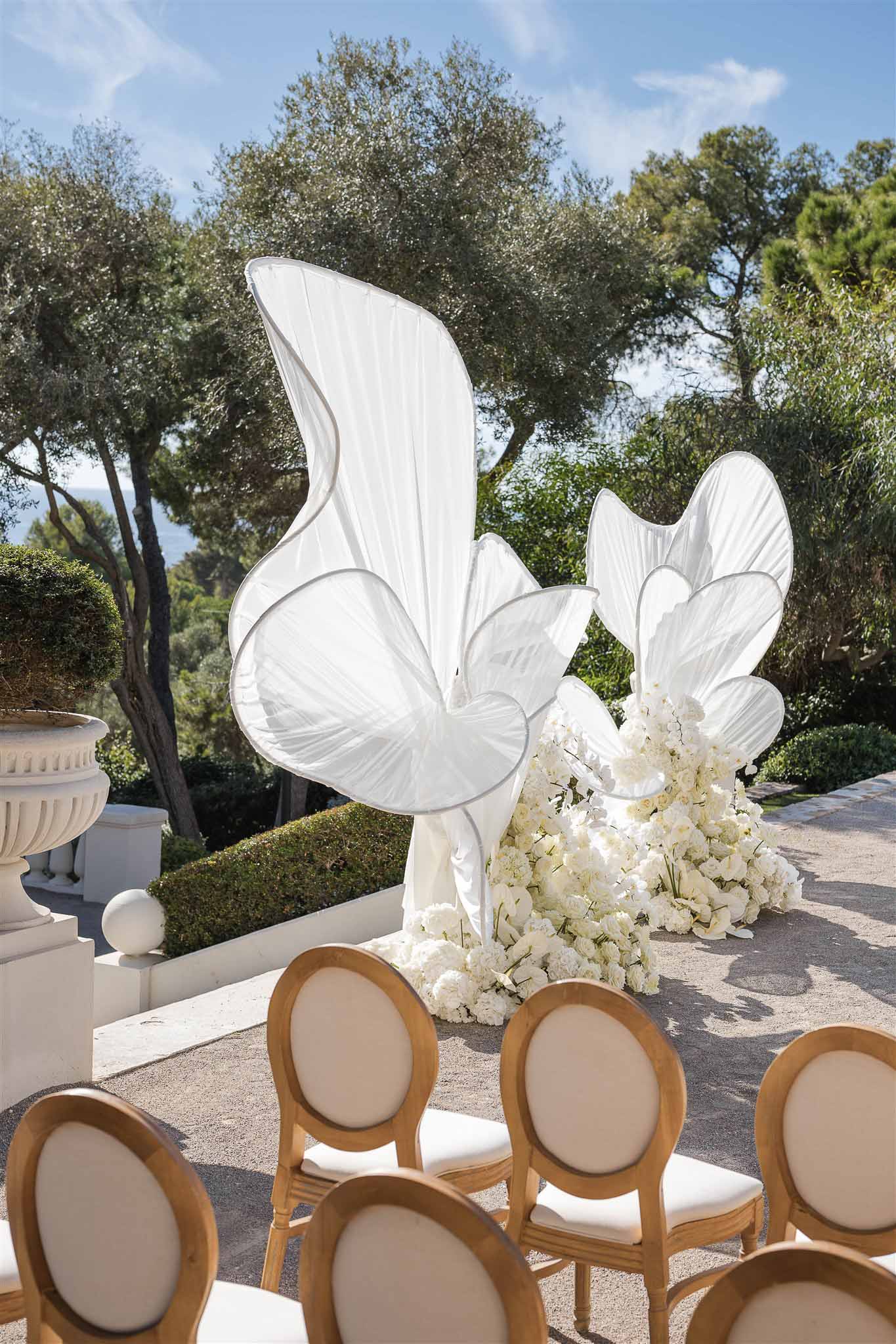 Outdoor ceremony terrace with white butterfly fabric sculptures, gold Louis XVI chairs, and sea view