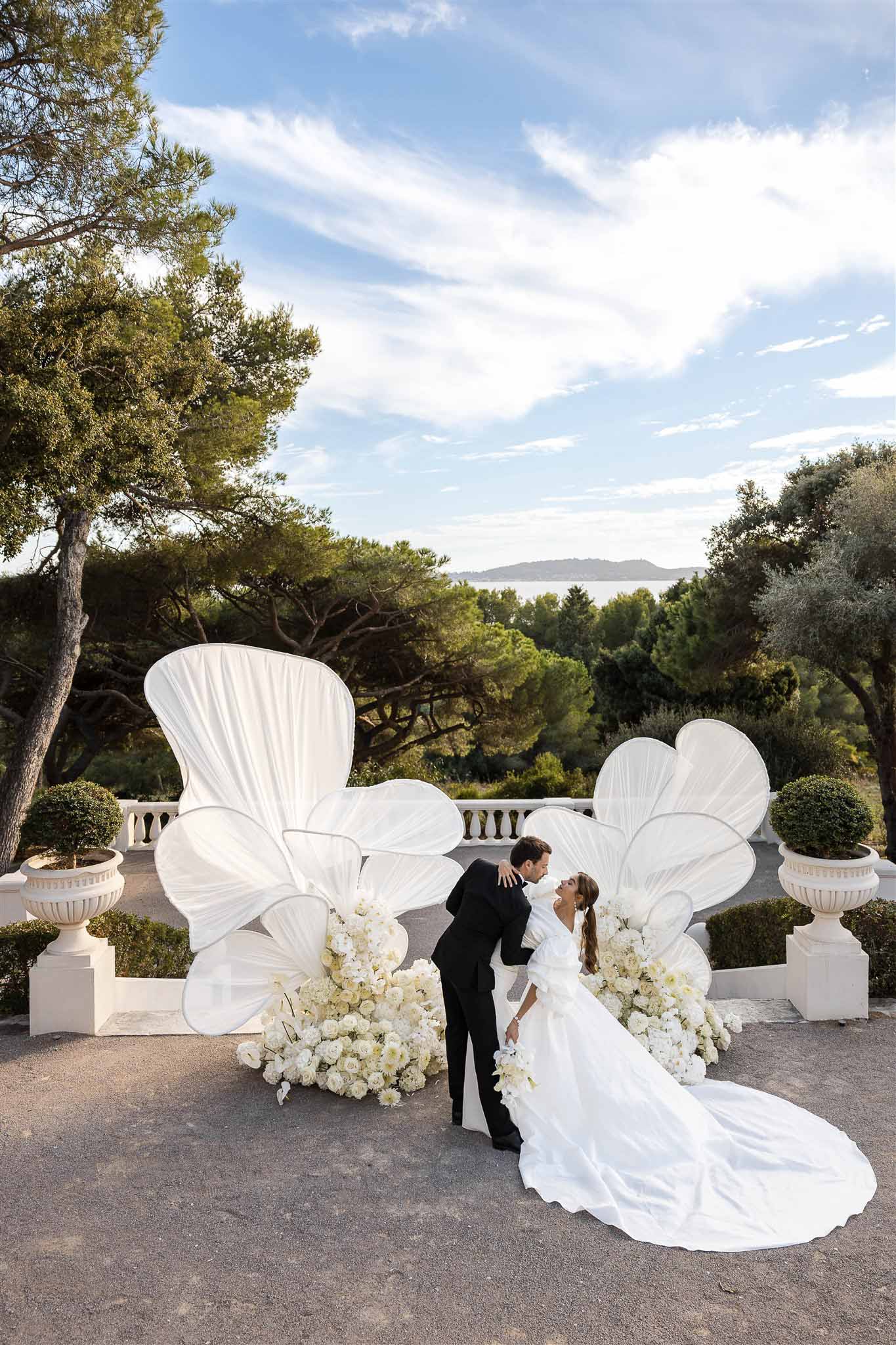 Bride with ruffled sleeves and long train kissing groom before sculptural white panels and sea view terrace