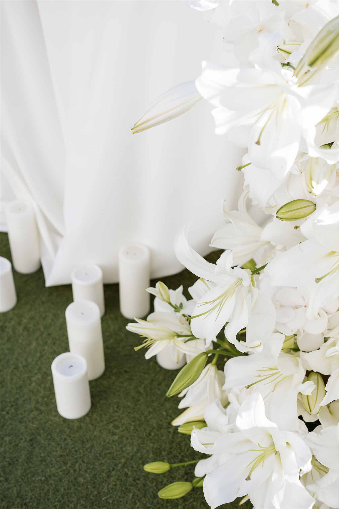 Ceremony altar with white oriental lilies, pillar candles, and flowing white fabric drape on lawn