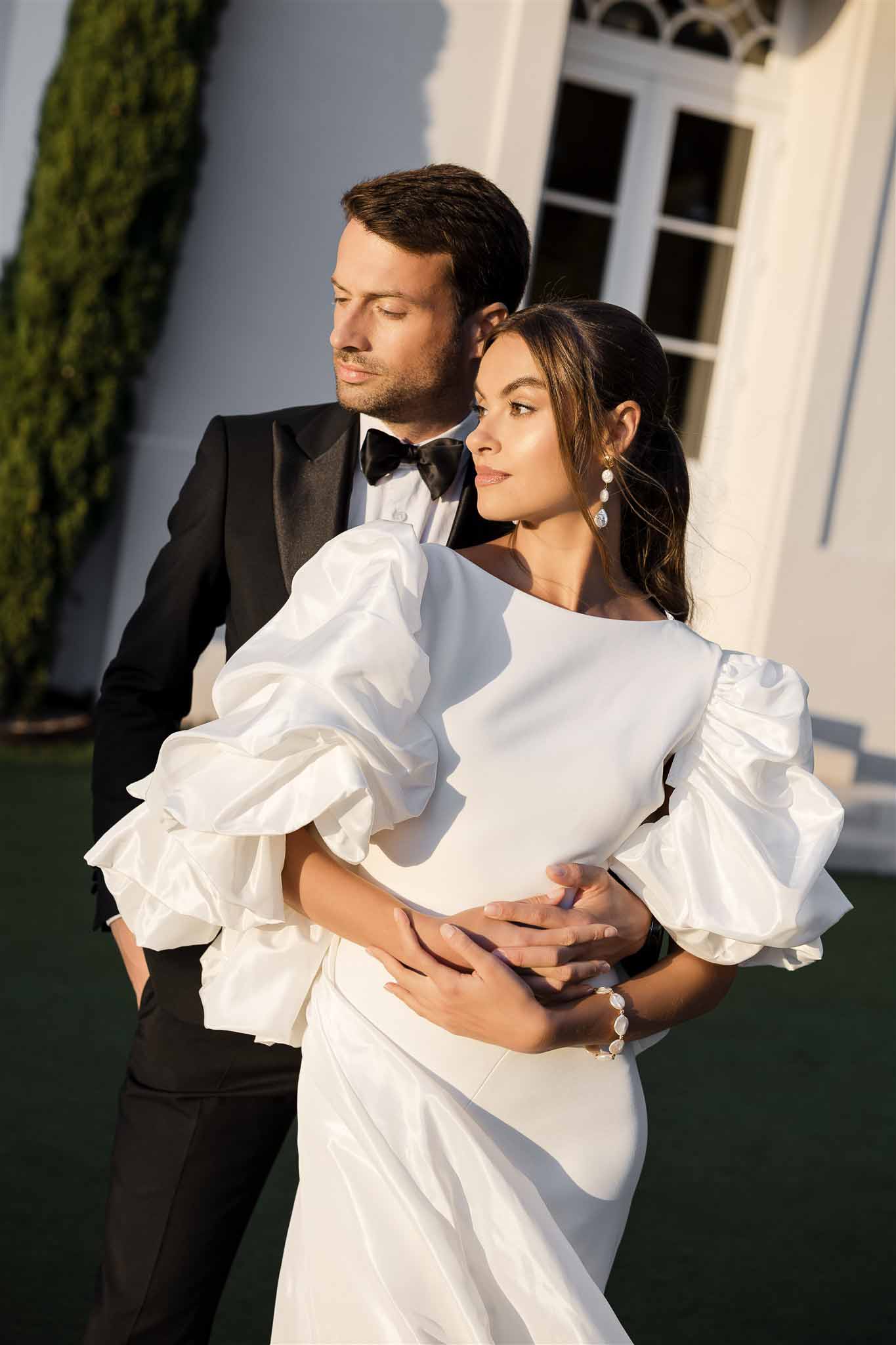 Close-up groom embracing bride in gown with oversized ruffled puff sleeves crystal earrings in warm afternoon light