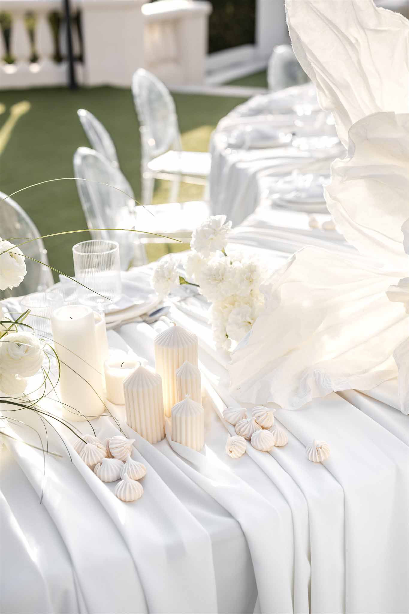 All-white monochromatic tablescape with pillar candles, meringues, ranunculus, and ghost chairs