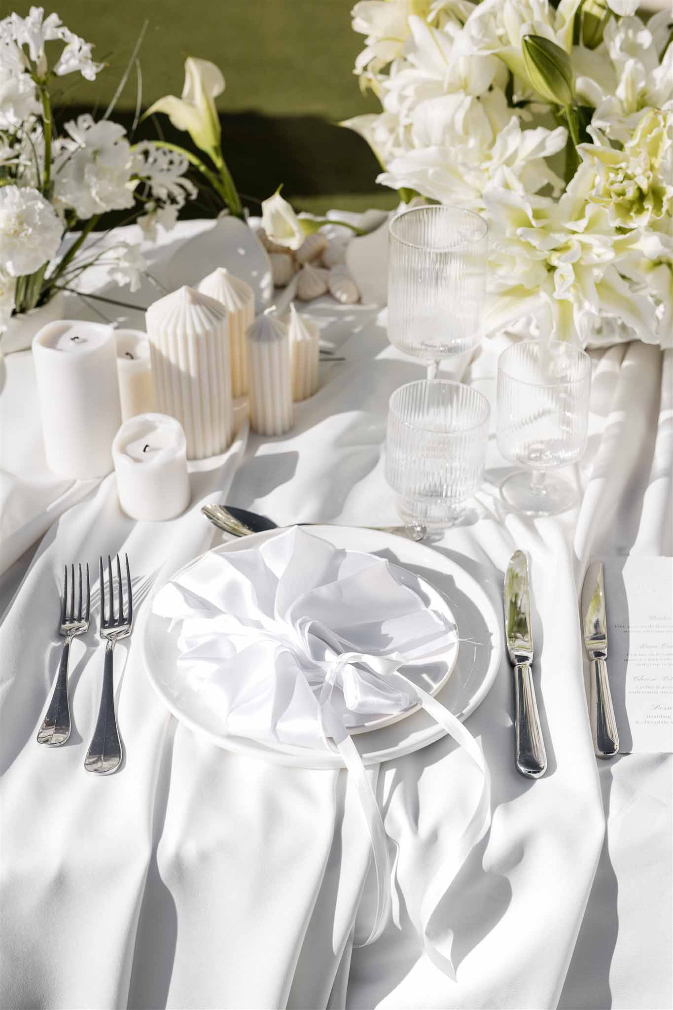 All-white place setting with organza ribbon napkin, sculptural candles, and calla lily arrangement