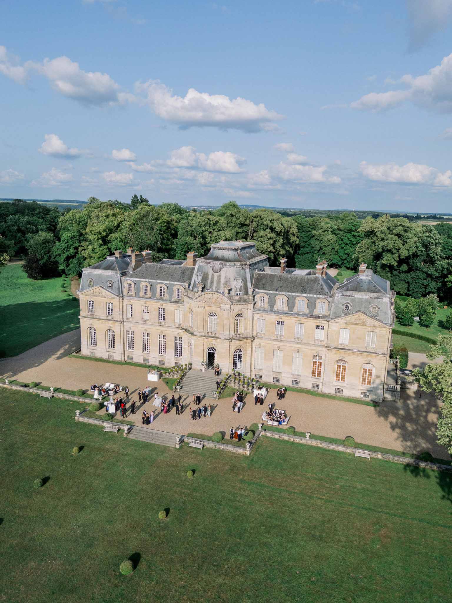 Aerial drone view of cocktail hour on the gravel forecourt of a French chateau with 60-80 guests