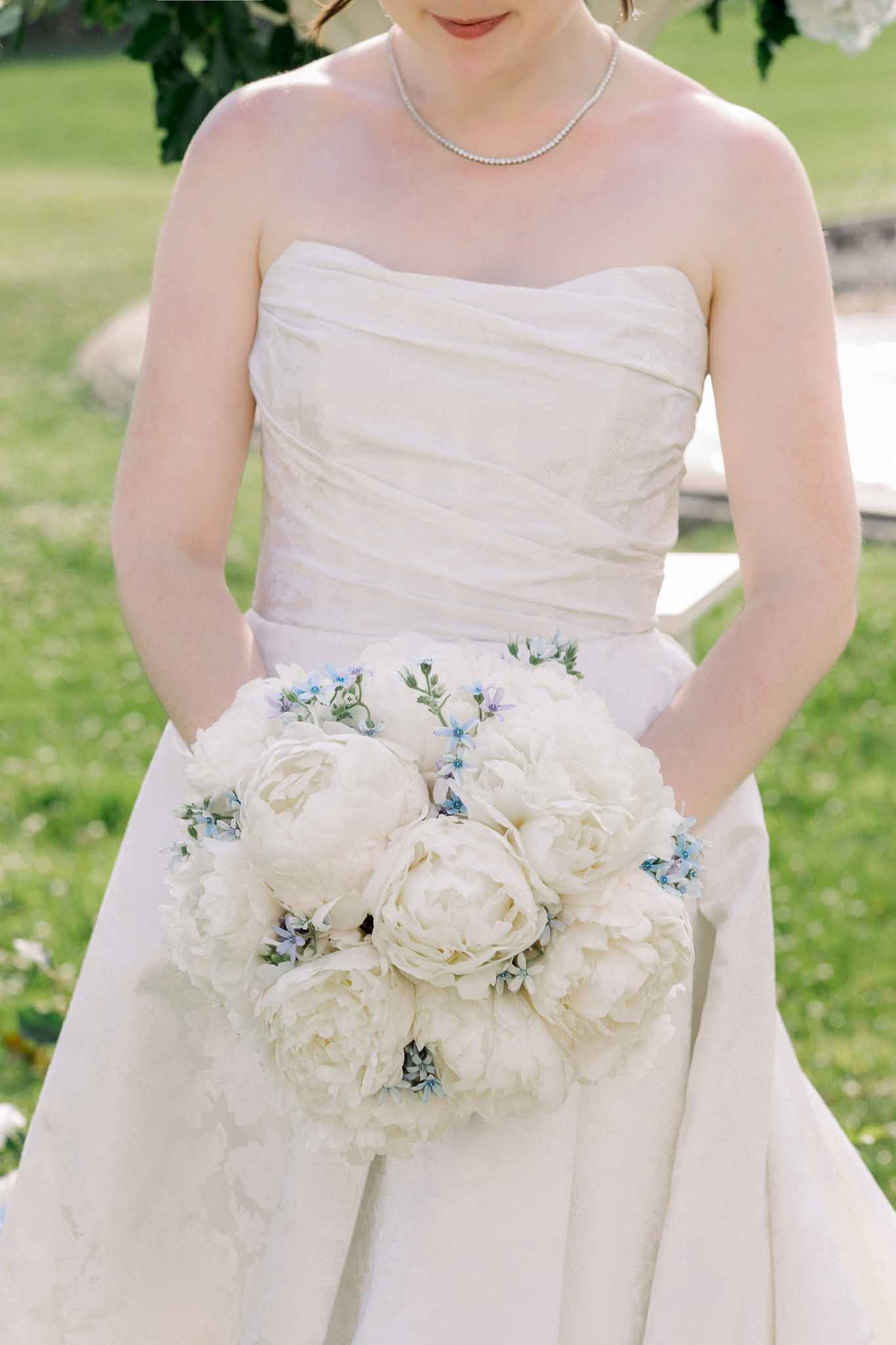 Bride holding rounded bouquet of white peonies with pale blue forget-me-nots