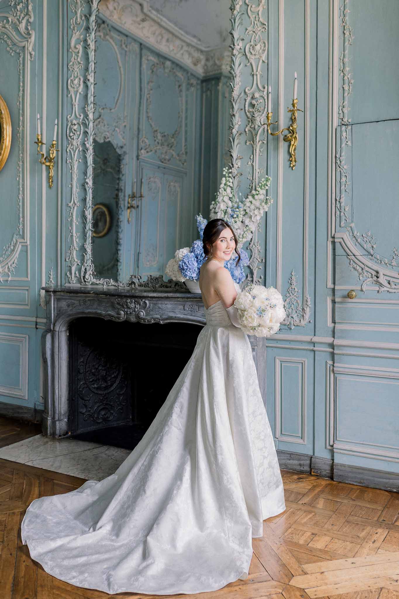 Bride in ivory strapless ball gown with cathedral train holding ivory rose and blue hydrangea bouquet in chateau salon