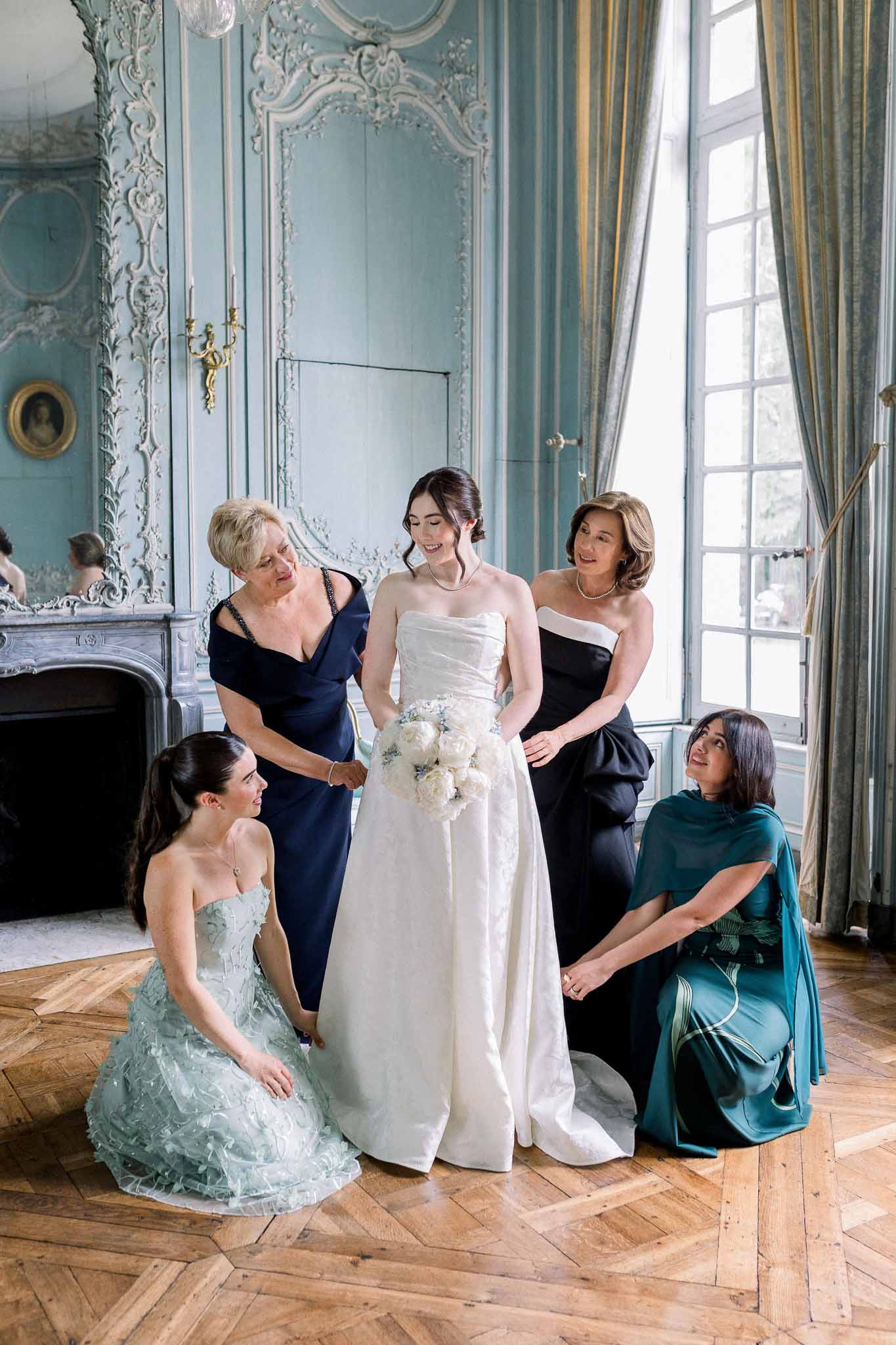 Bride with white peony bouquet and four women in navy mint and teal gowns in ornate chateau salon