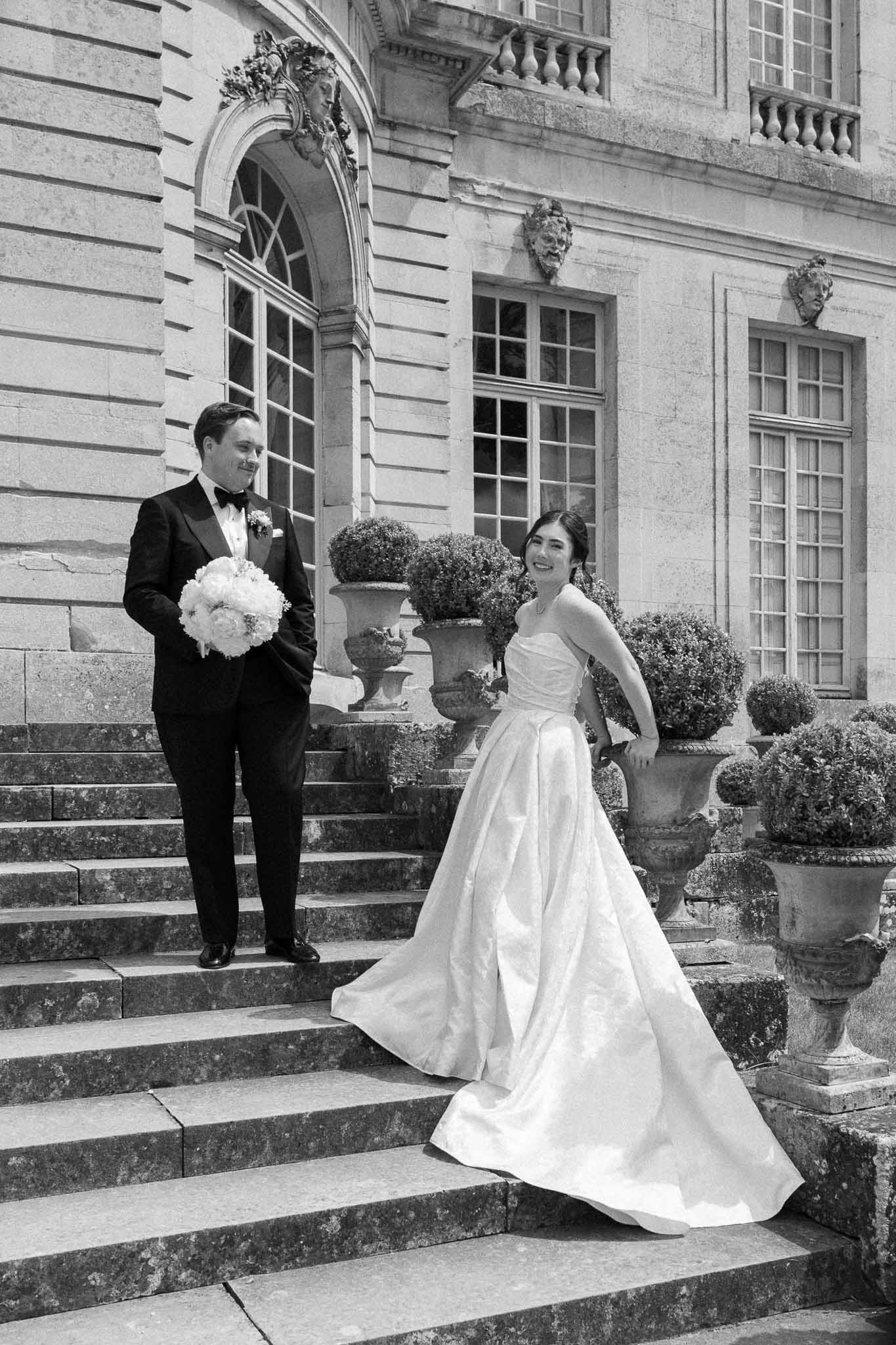 Black-and-white couple portrait on chateau stone staircase, bride in strapless ballgown, groom in tuxedo