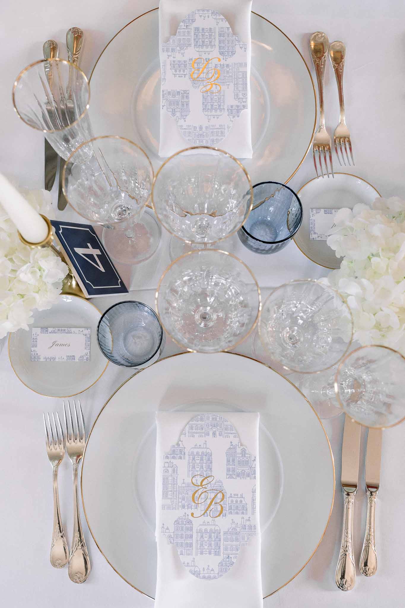 Overhead place settings with gold-rimmed plates blue toile napkins monogram and crystal coupe glasses