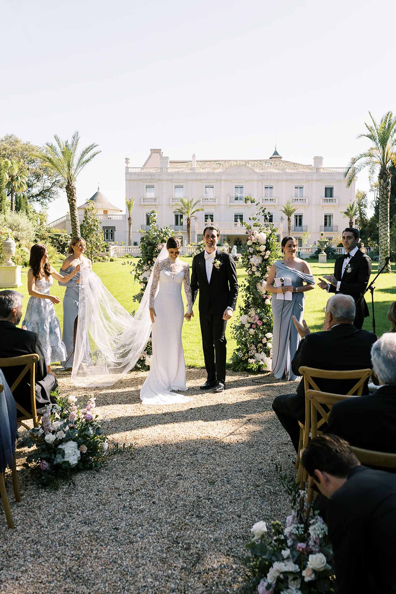 Bride and groom walking up the aisle hand in hand after ceremony with bridesmaids in dusty blue at neoclassical chateau