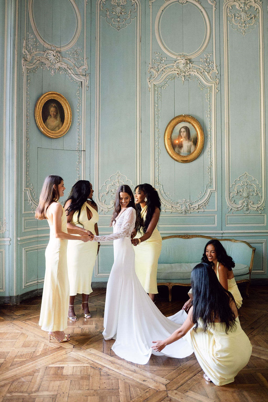 Bride with four bridesmaids in butter-yellow midi dresses arranging train in blue-grey boiserie salon