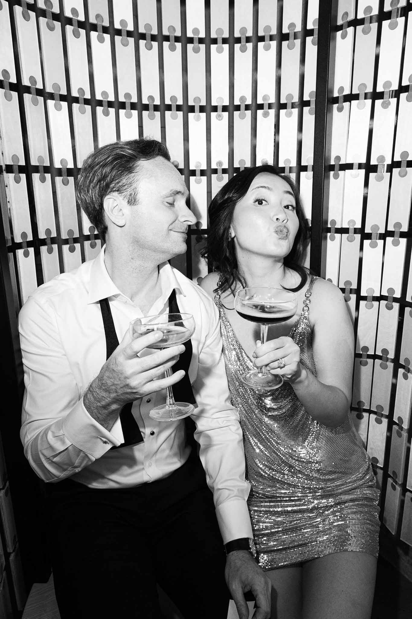 Black and white couple posing playfully at reception photo booth with cocktail glasses
