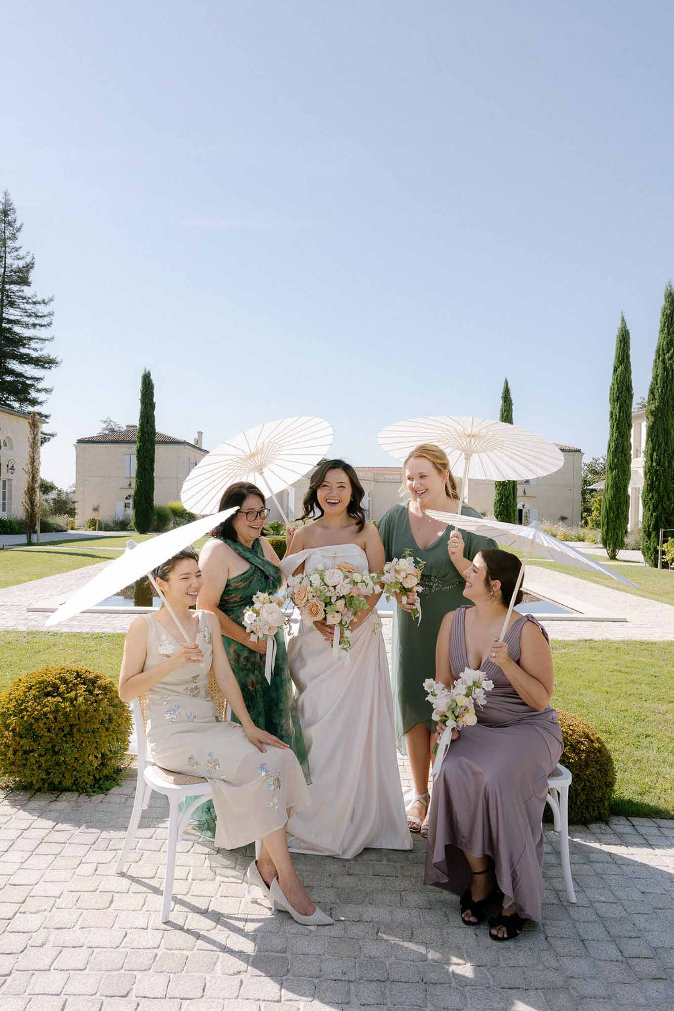Bride with four bridesmaids in mismatched attire holding parasols on chateau terrace