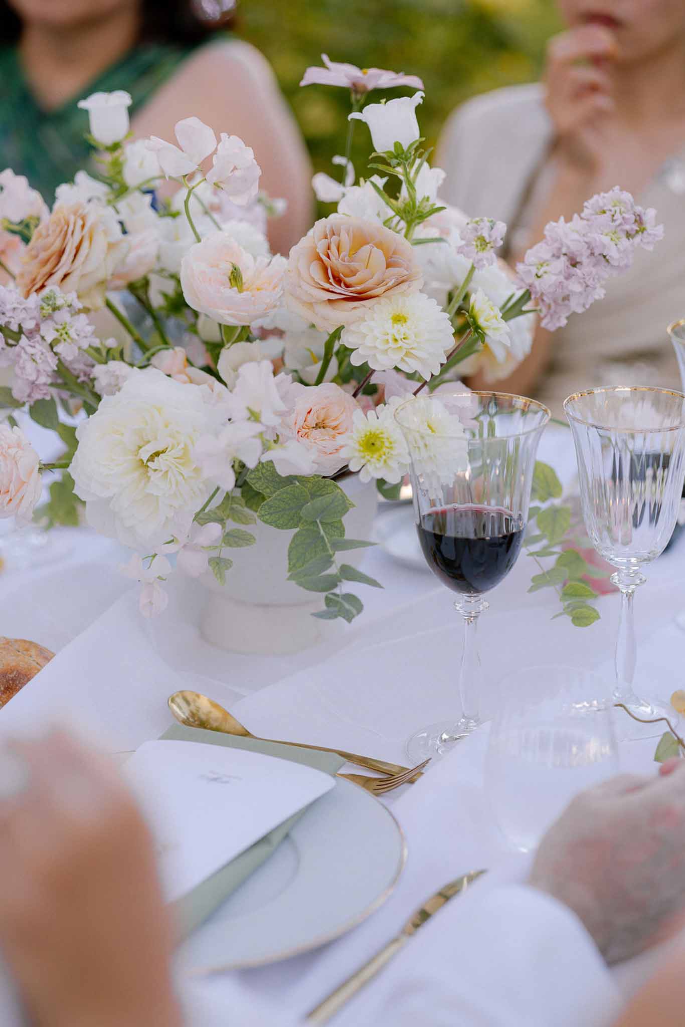 Reception table detail with blush and peach roses in white vessel, sage chargers, and gold-rimmed crystal glasses