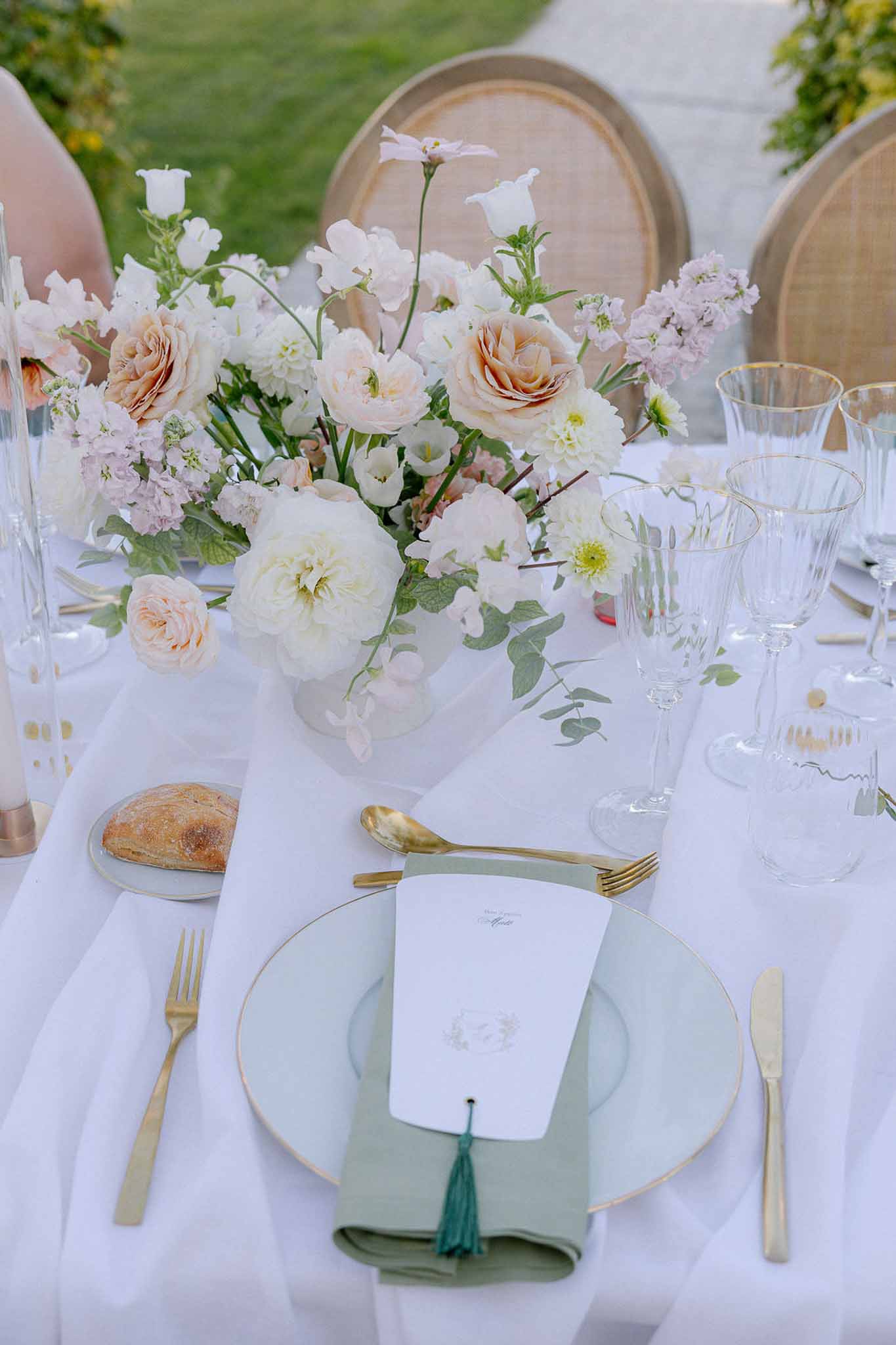Sage green charger plate with gold rim, garden rose centerpiece, and gold flatware on white linen