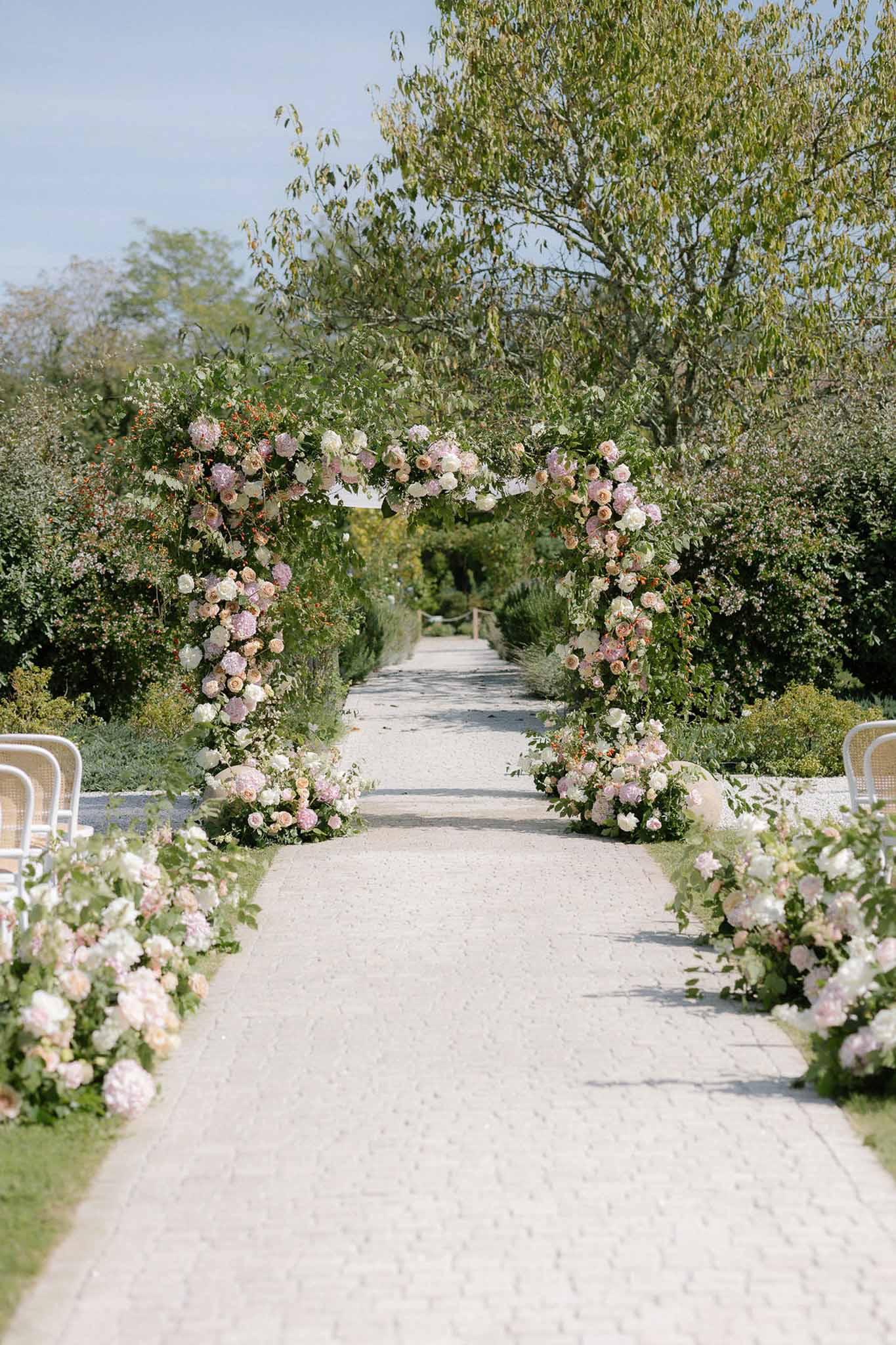 Circular floral arch of blush hydrangeas and ivory roses with ground-level peony aisle arrangements