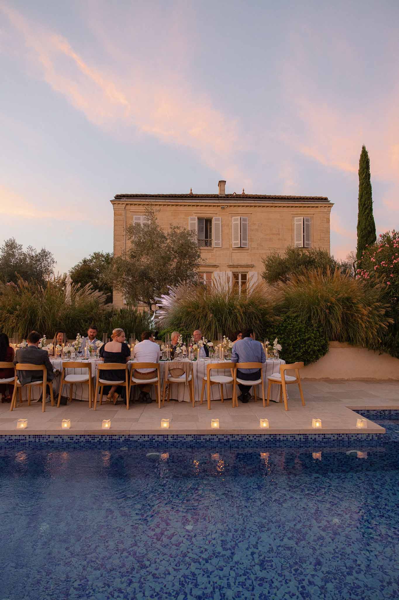 Poolside reception dinner at dusk in front of French manor with votive candles reflecting in water