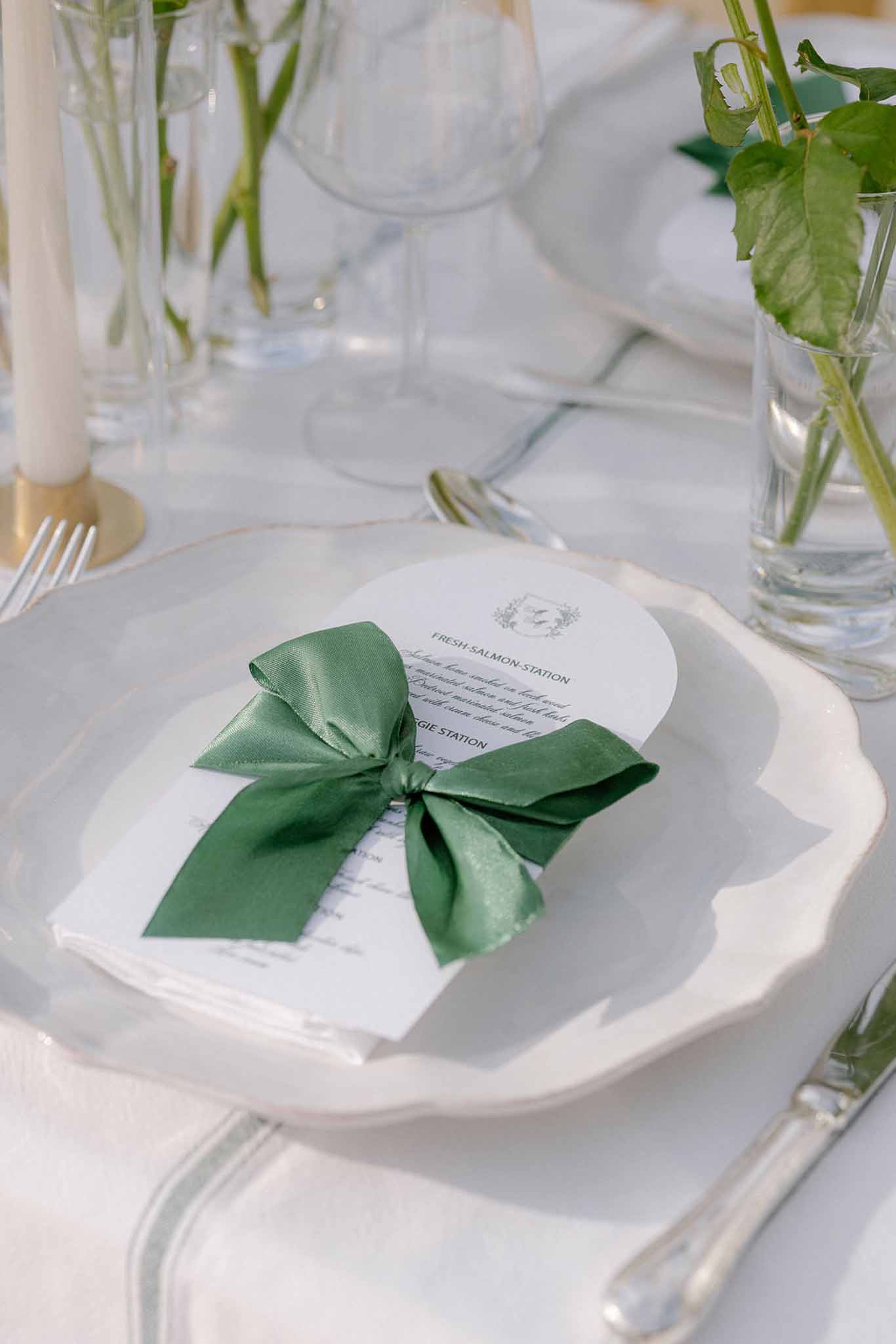 White scallop-edge charger with circular menu card tied with forest green satin ribbon bow