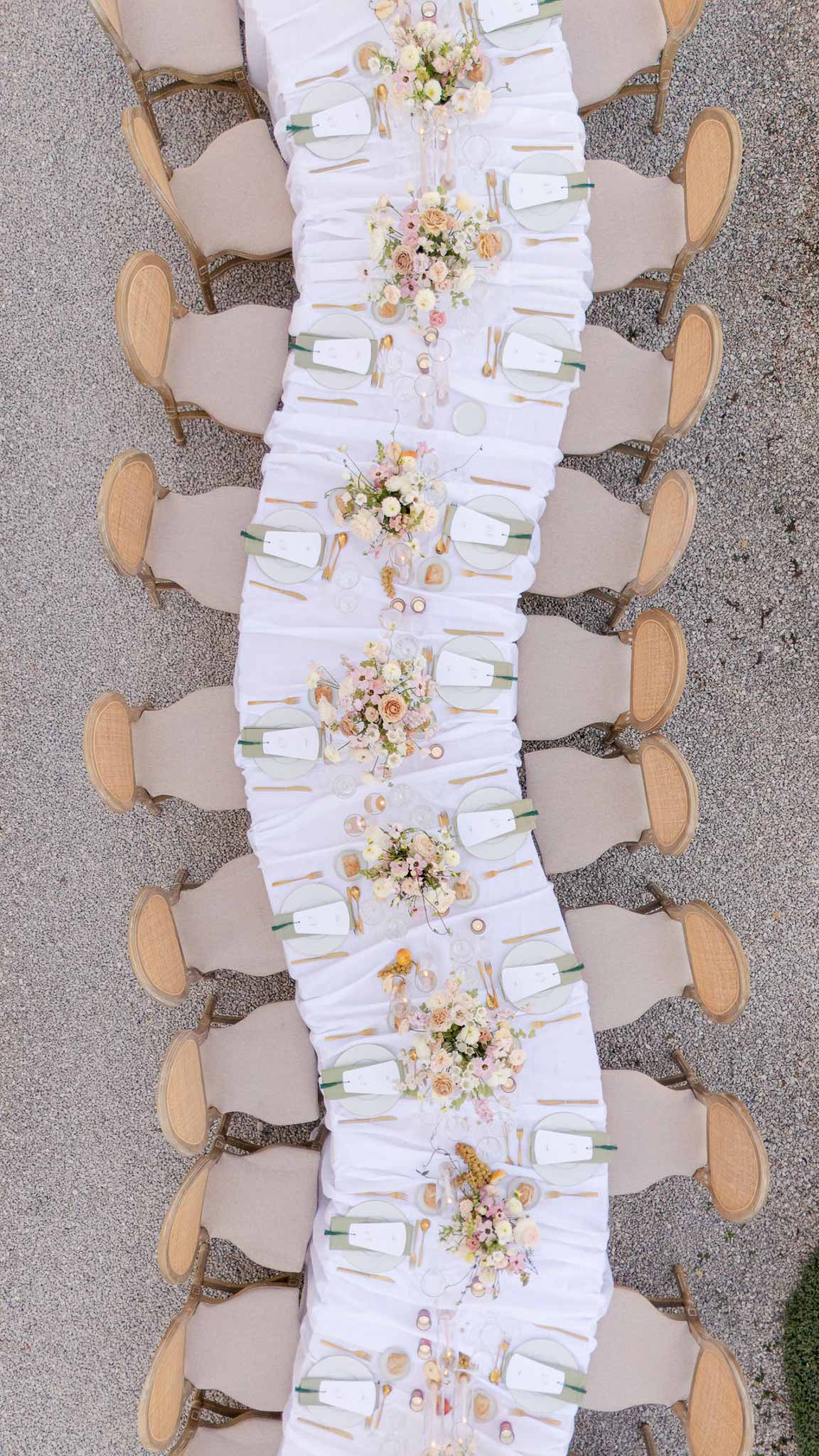 Aerial view of reception table with sage charger plates, blush roses, and cane-back chairs
