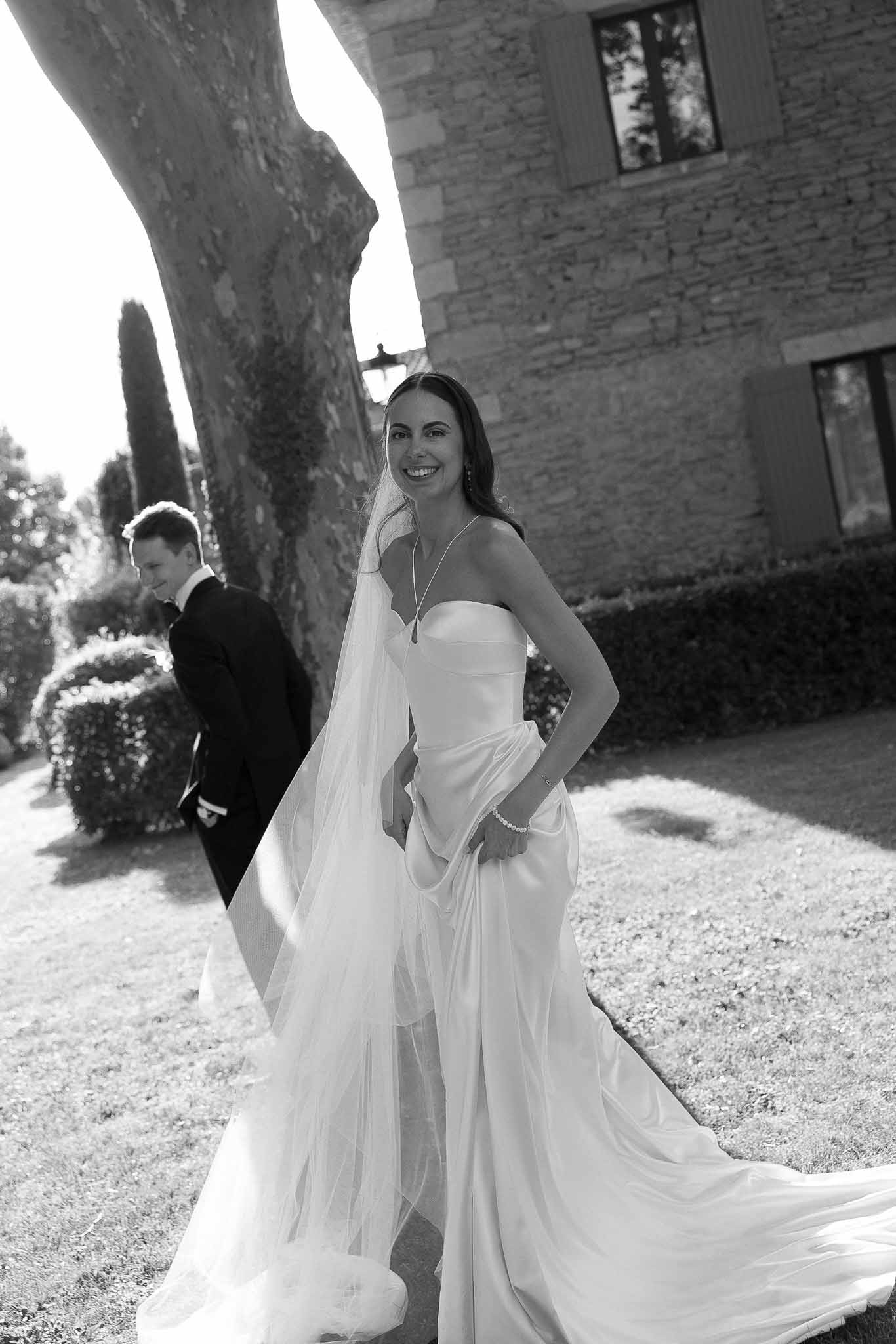 Black-and-white portrait of bride in strapless satin gown and cathedral veil with groom in tuxedo on chateau grounds