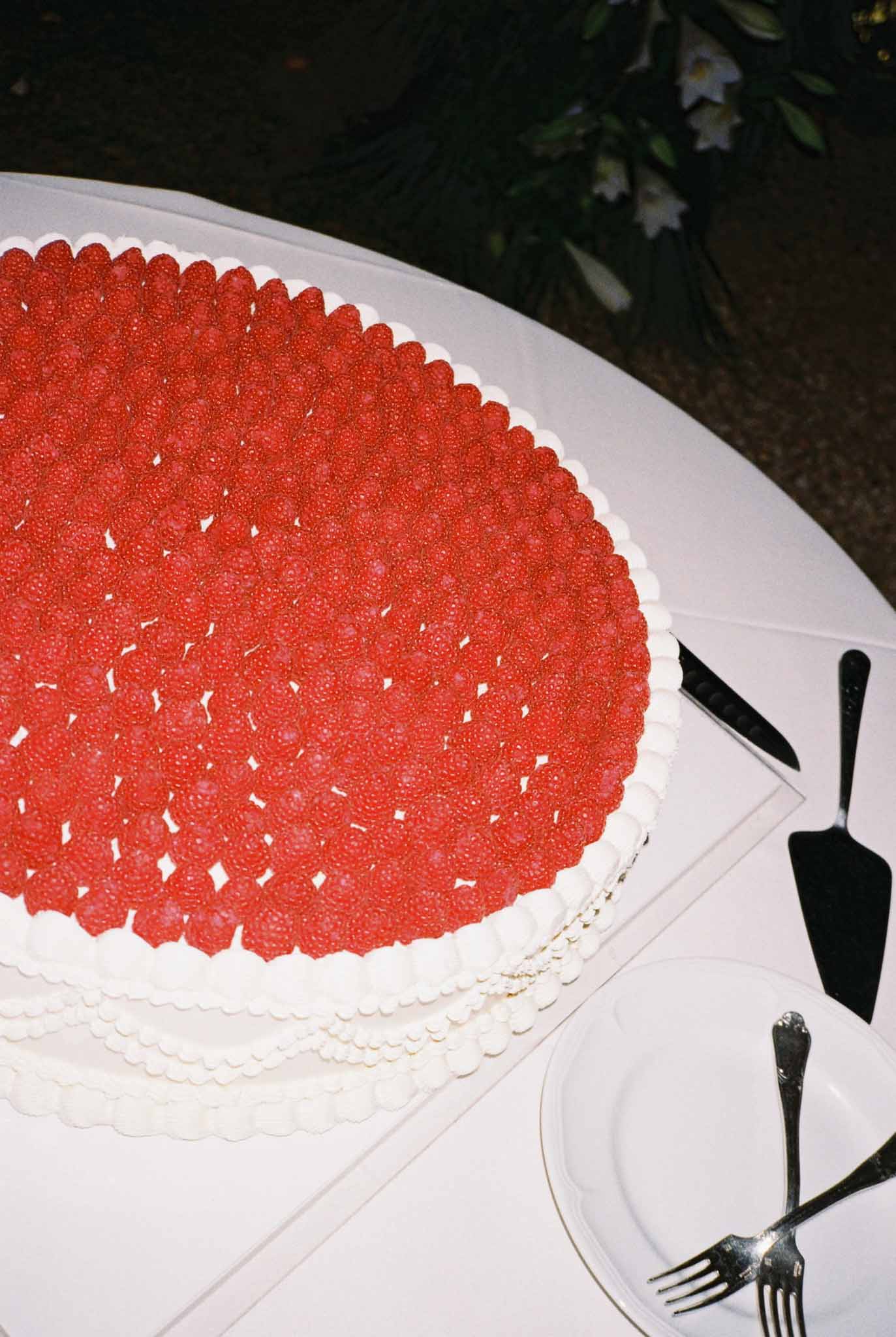 Oval wedding cake covered in fresh raspberries with piped white cream scallop border on a linen-draped table