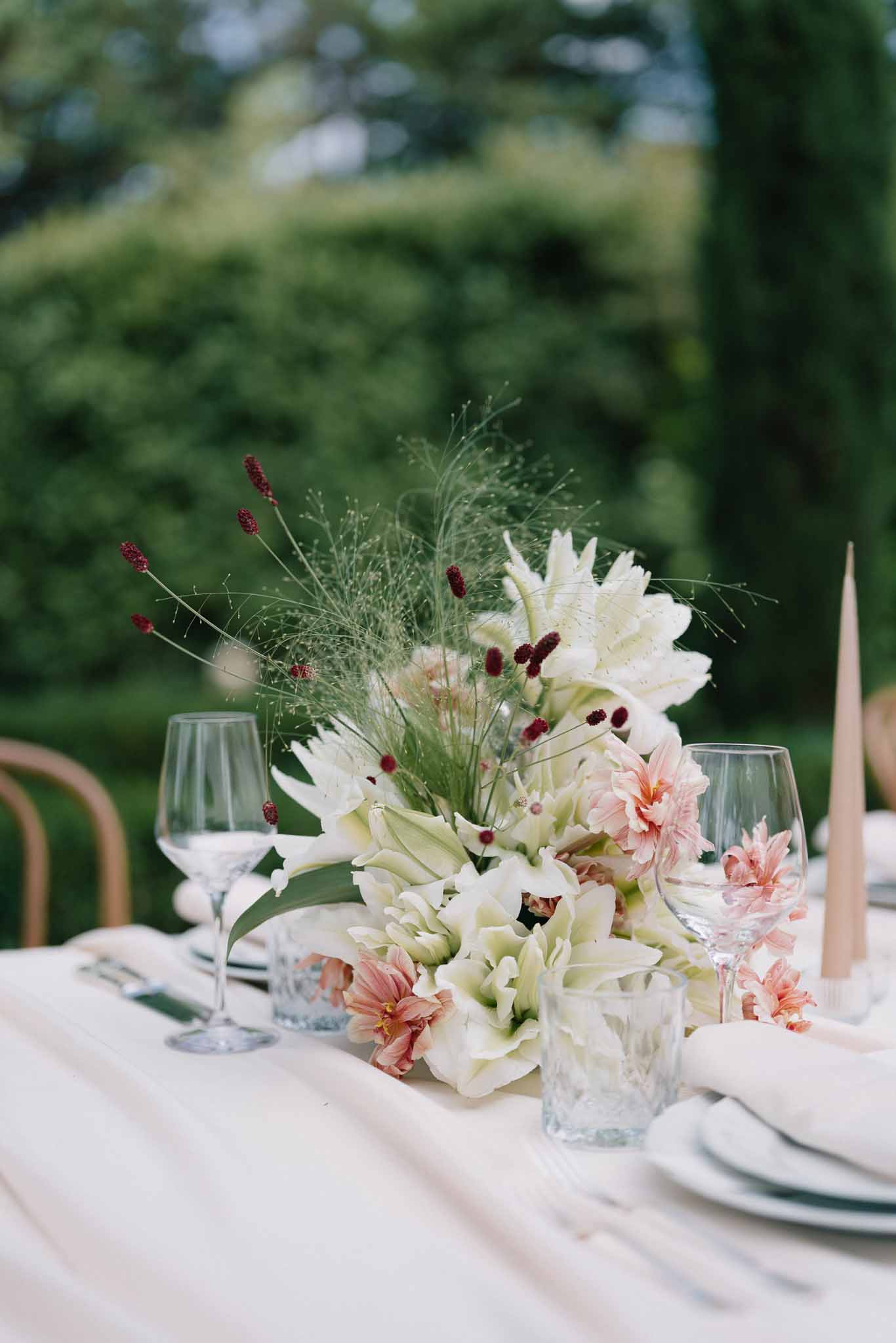 Low centerpiece of cream amaryllis blush dahlias and burgundy sanguisorba with taper candles