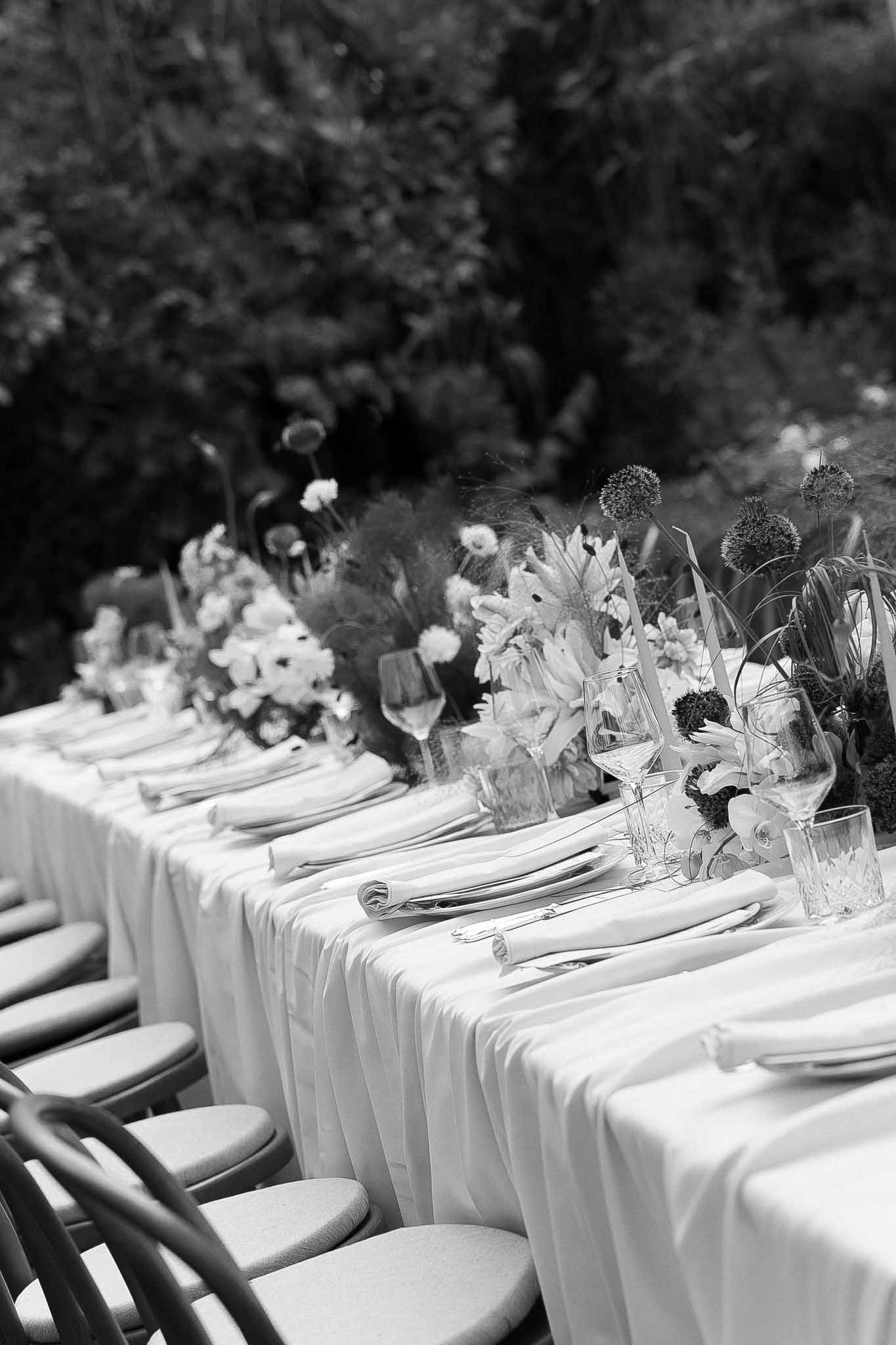 Black and white low-angle view of outdoor reception table with floral centerpieces and taper candles