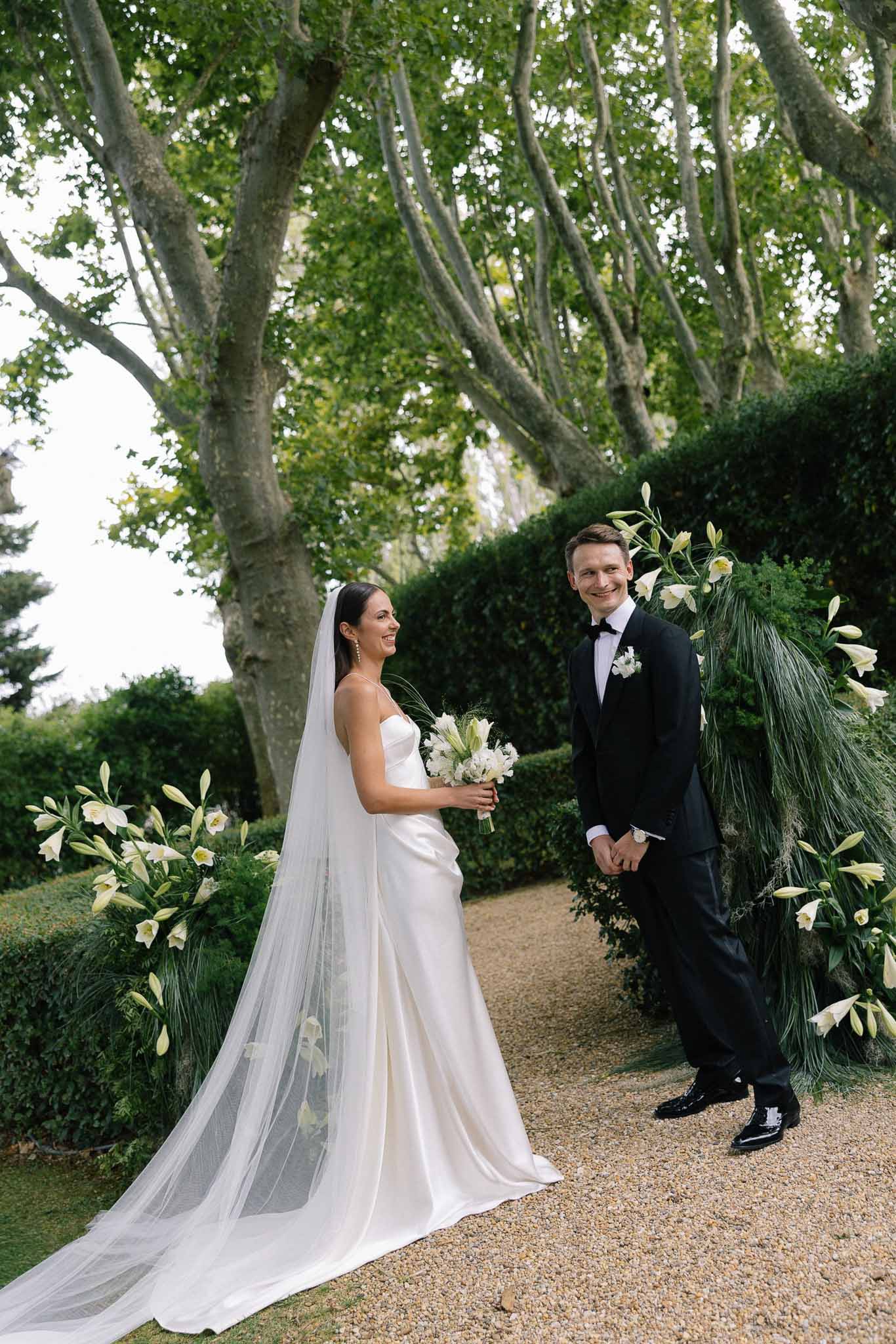 Couple smiling before circular greenery and white lily arch with matching tall arrangements