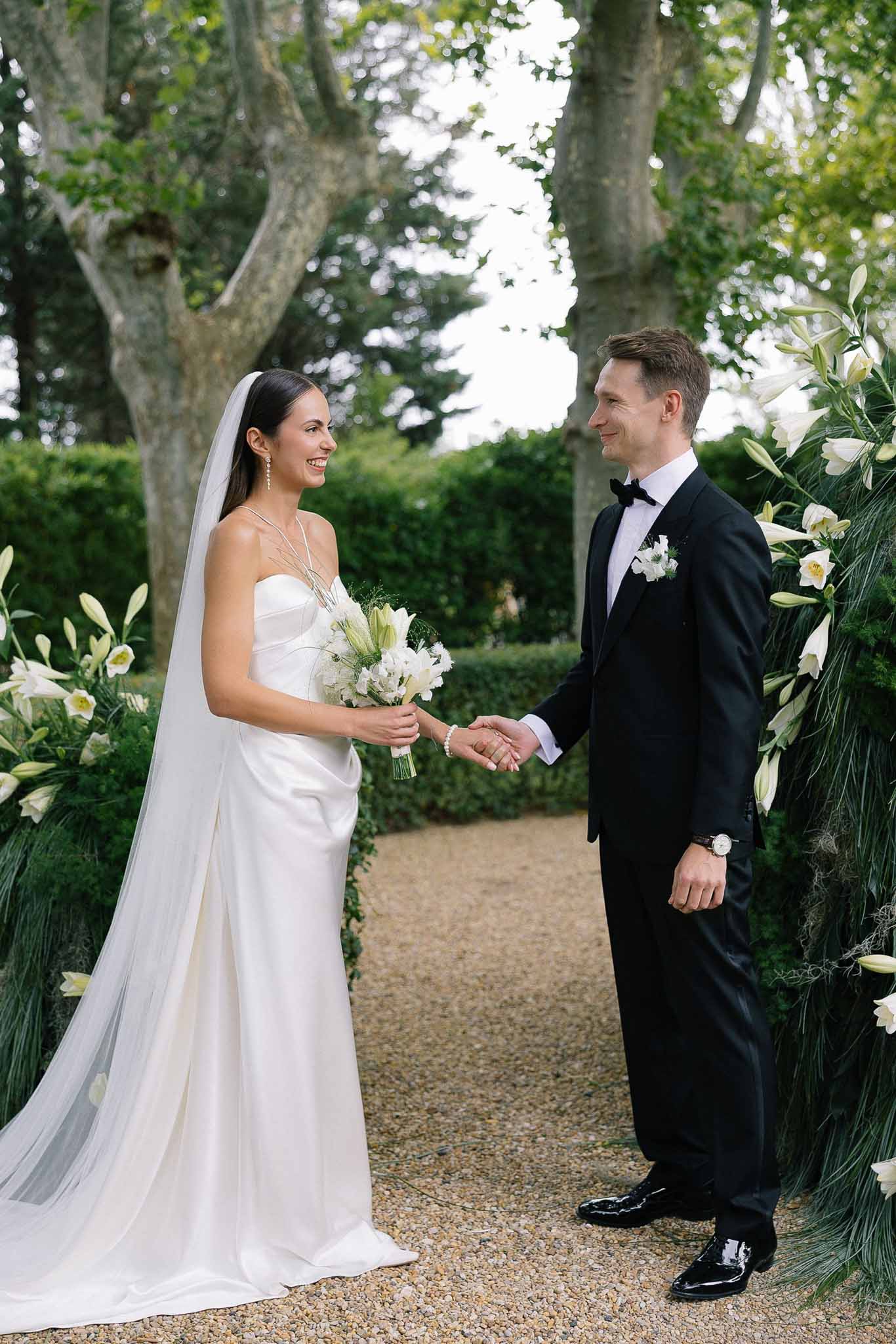 Couple holding hands at outdoor altar flanked by white lily column arrangements in formal garden