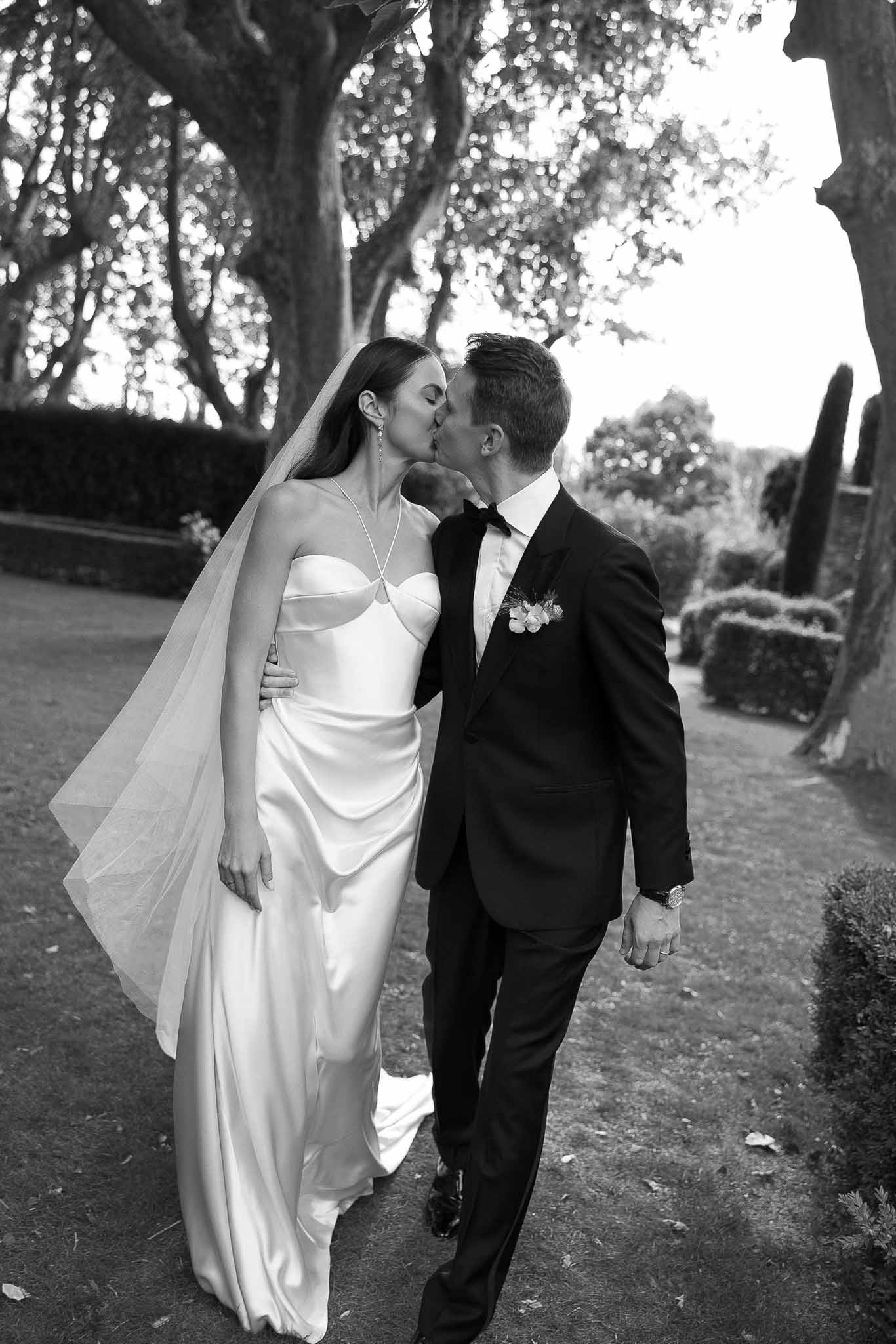 Black and white couple kissing mid-stride in formal garden with hedgerows and topiary