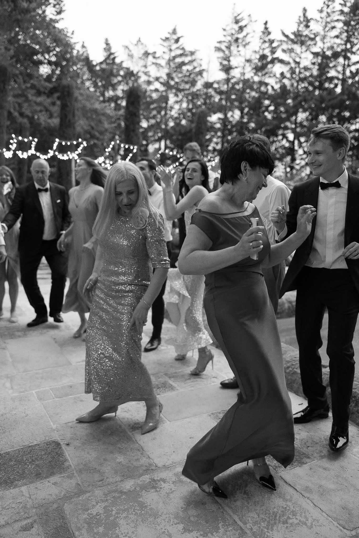 Guests dancing energetically on outdoor terrace with string lights at evening reception in black and white