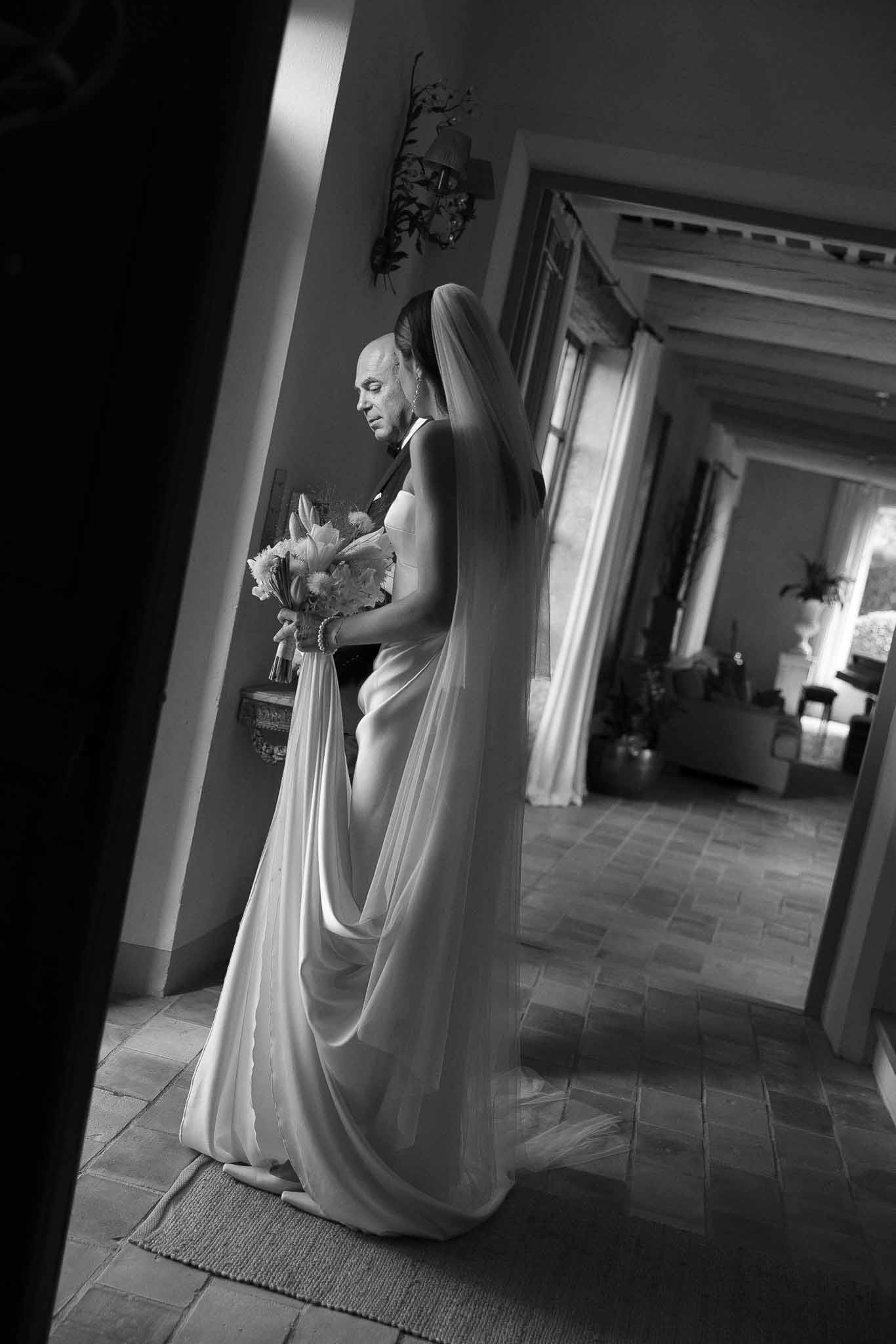 Black and white portrait of bride and father in tuxedo standing in doorway of stone mas interior