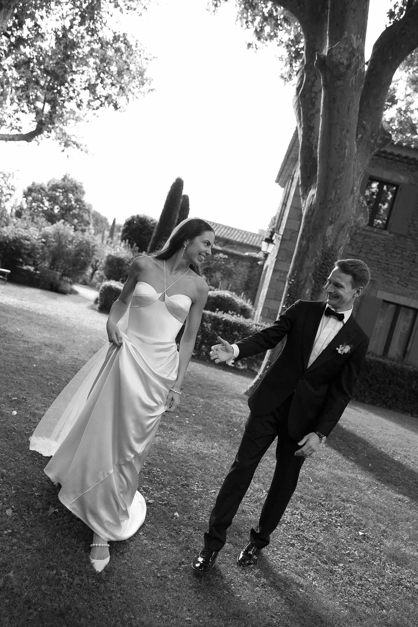 Black and white couple walking hand in hand across manor lawn with cypress trees and hedges behind