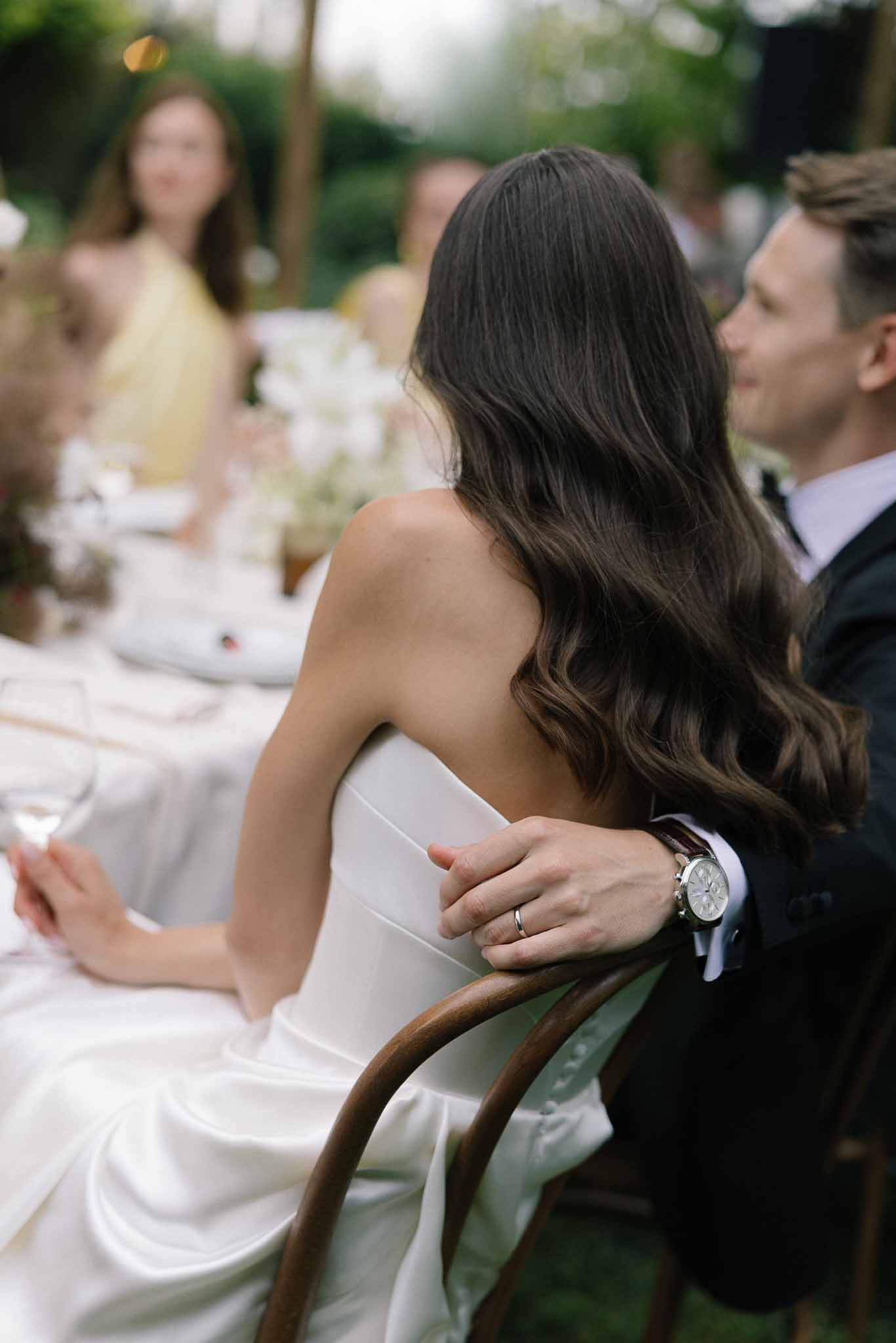 Bride in strapless ivory gown and groom in dark suit seated together at outdoor reception dinner table