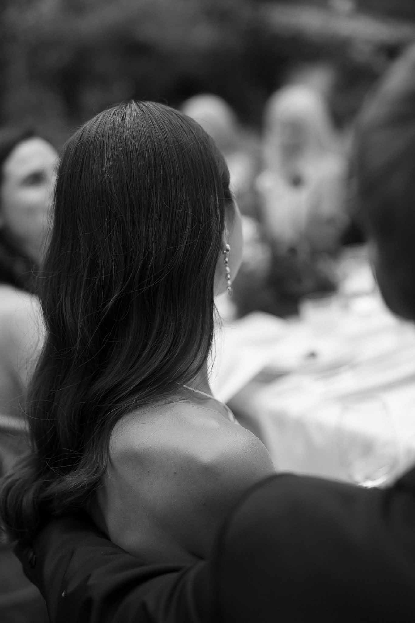 Black and white close-up from behind of woman with loose waves and drop earring at wedding with blurred background