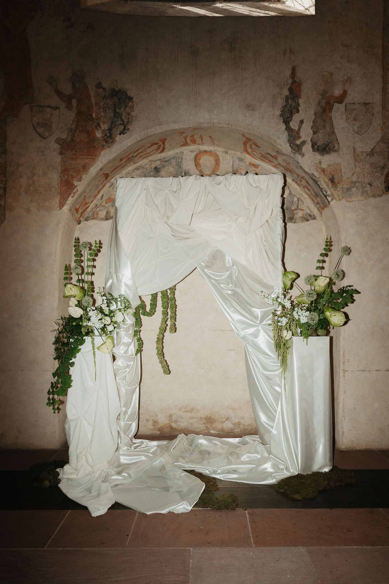 White ranunculus and anthurium altar installation with ivory satin draping in Romanesque stone chapel