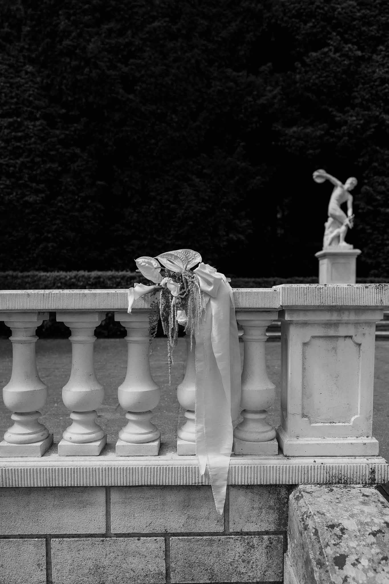 Black and white bridal bouquet with tropical leaves and calla lilies on stone balustrade with statue