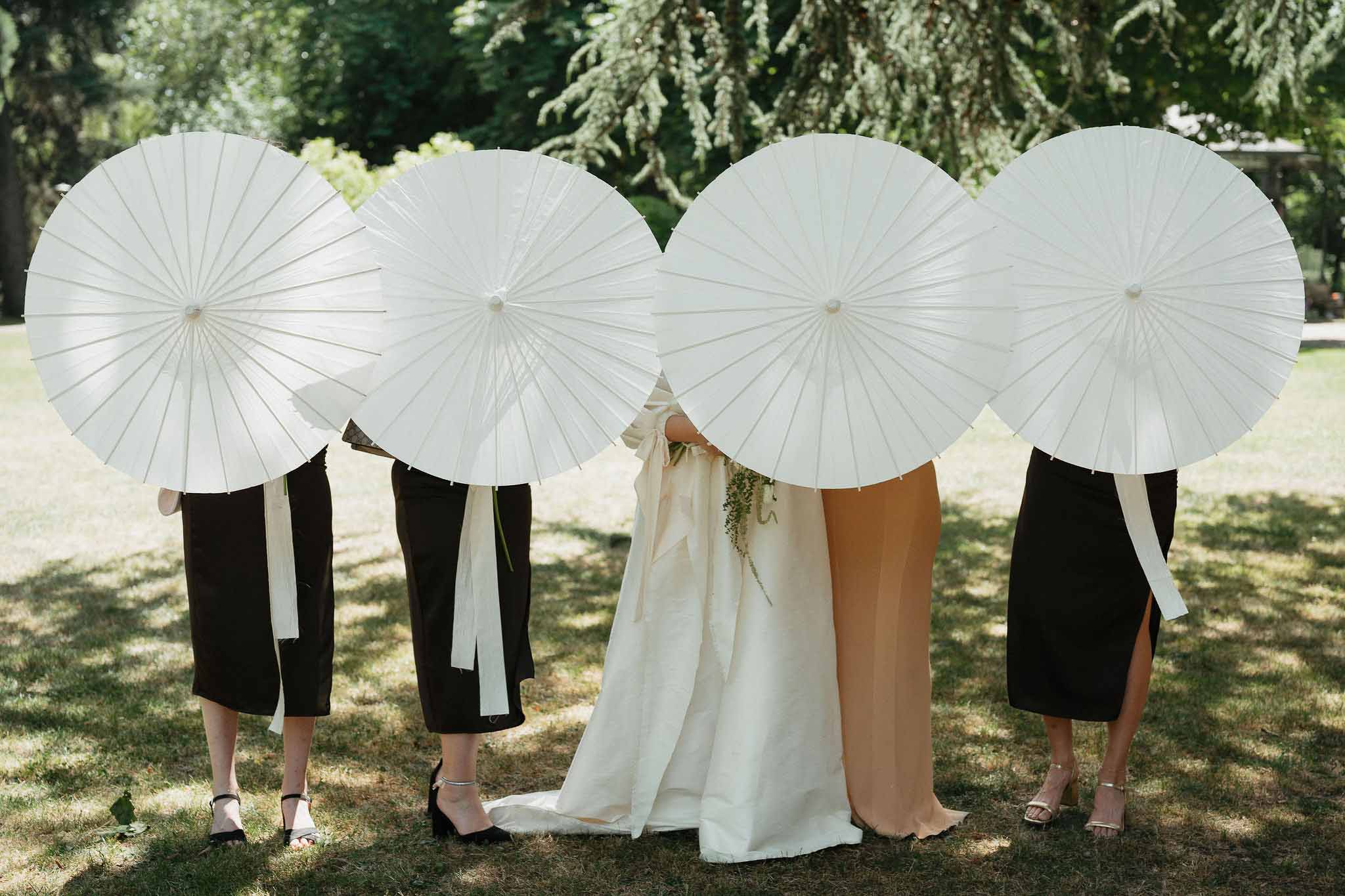 Bride and three bridesmaids holding white paper parasols in a garden setting