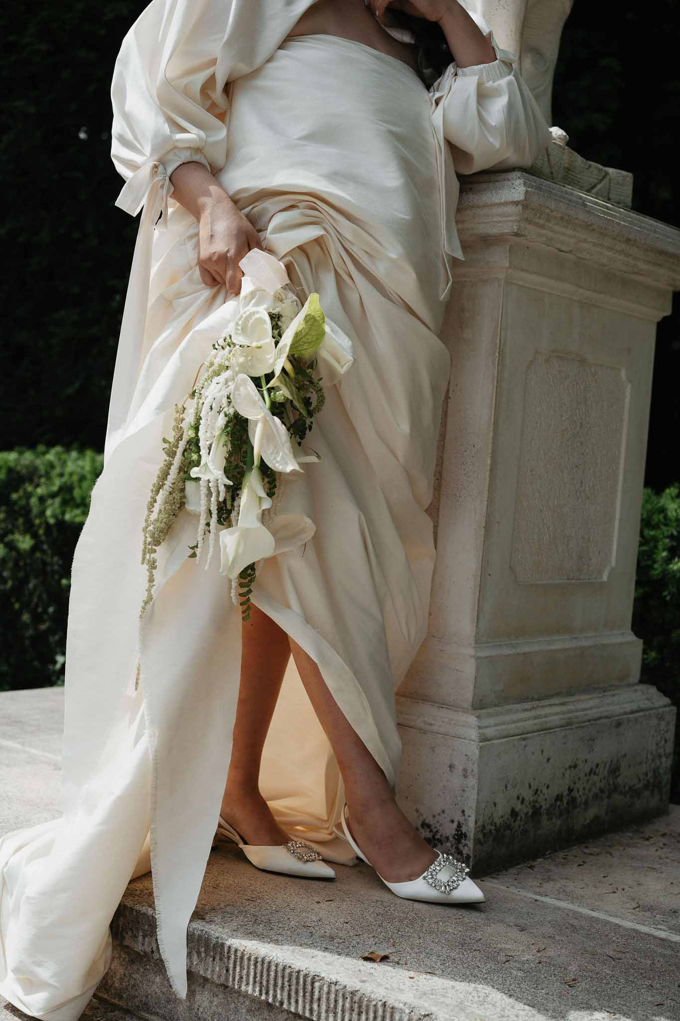 Close-up of champagne silk gown with billowing sleeves, crystal buckle flats, and cascading calla lily bouquet