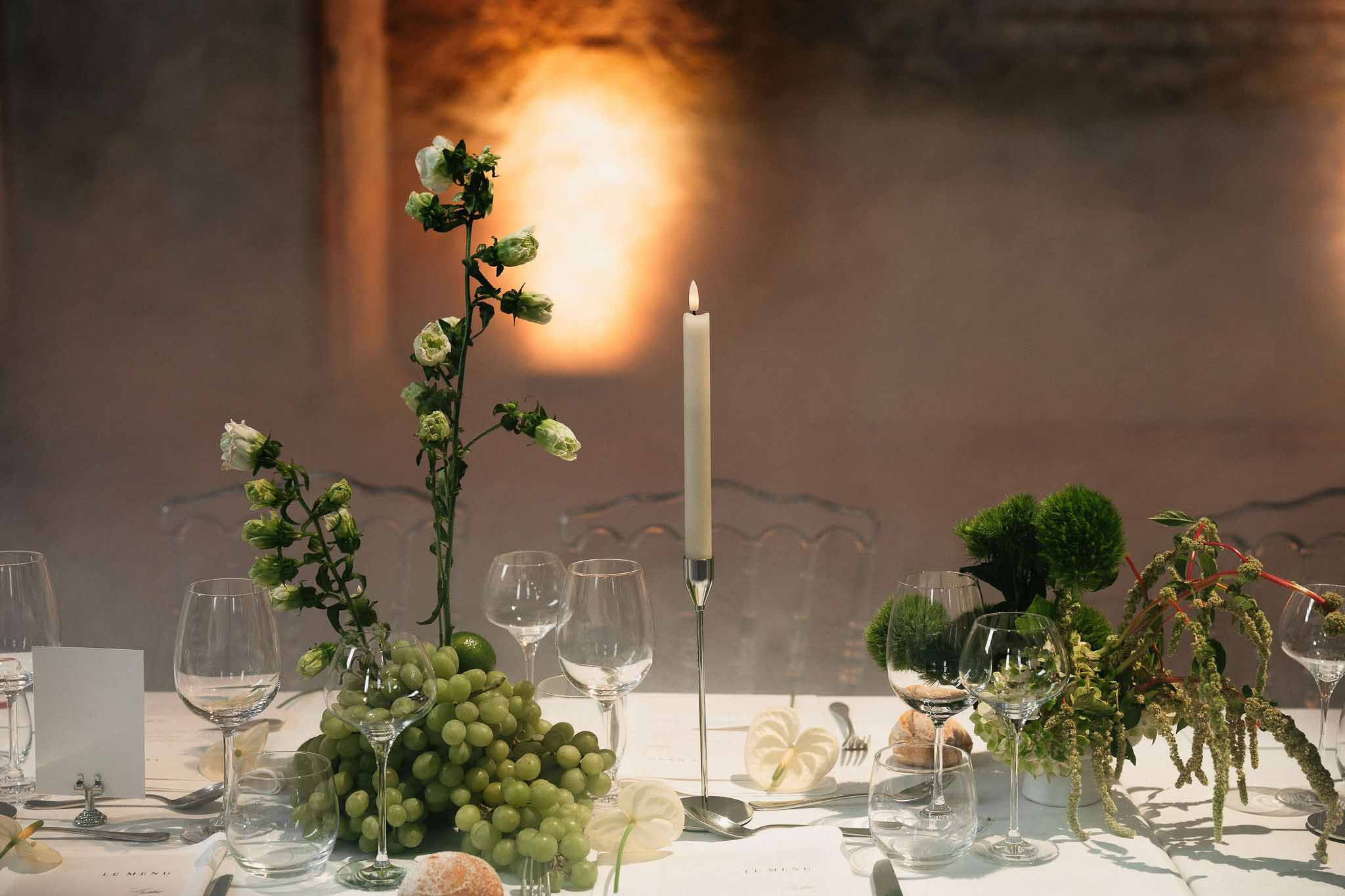 Reception table with green grape decor, white lisianthus, trailing amaranthus, and lit taper candle