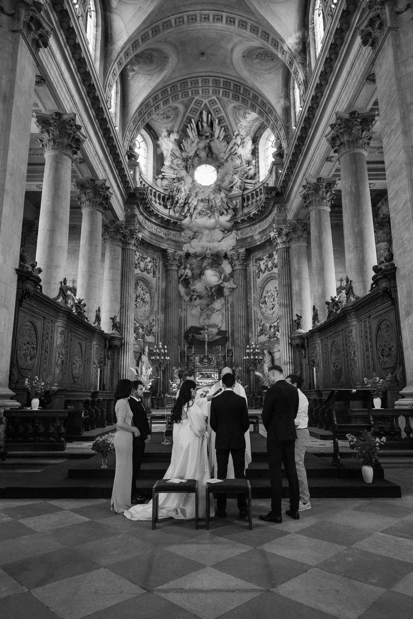 Black and white wide shot of couple at altar inside grand Baroque church with ornate dome and columns