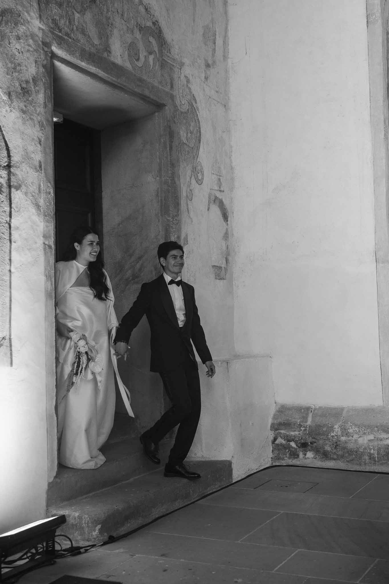 Black and white couple emerging from frescoed stone doorway laughing with bride in bishop-sleeve gown
