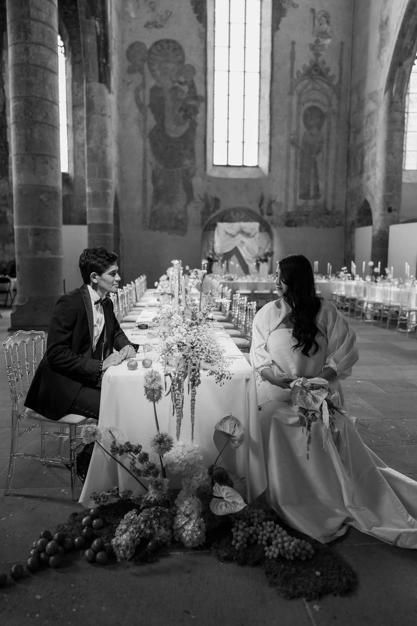 Black-and-white photo of couple at head table in Romanesque abbey with sculptural floral installation