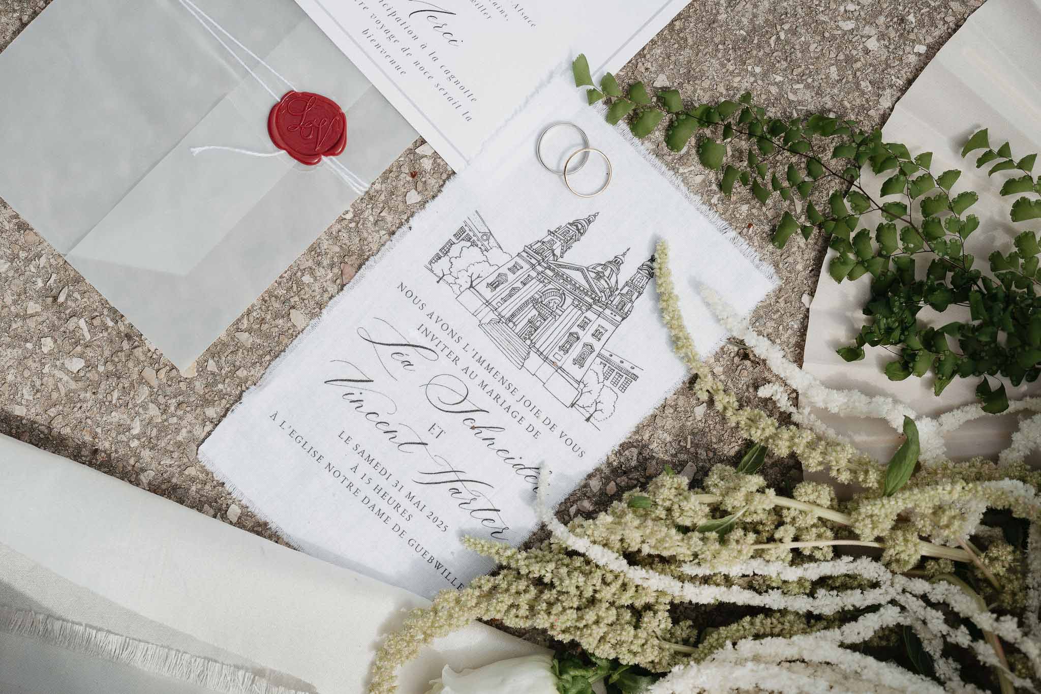 French wedding stationery flat lay with church illustration, red wax seal, and gold bands