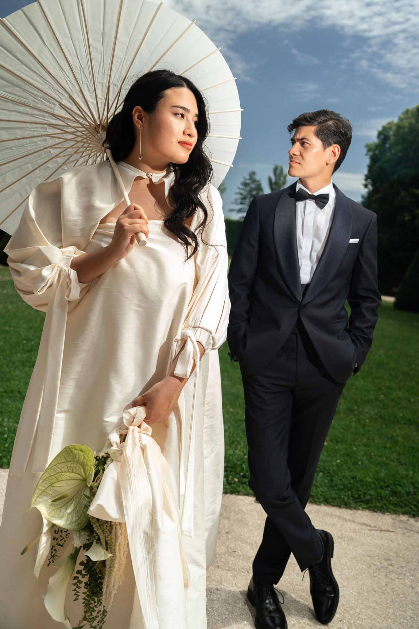 Couple on garden path with bride carrying white calla lily bouquet and paper parasol