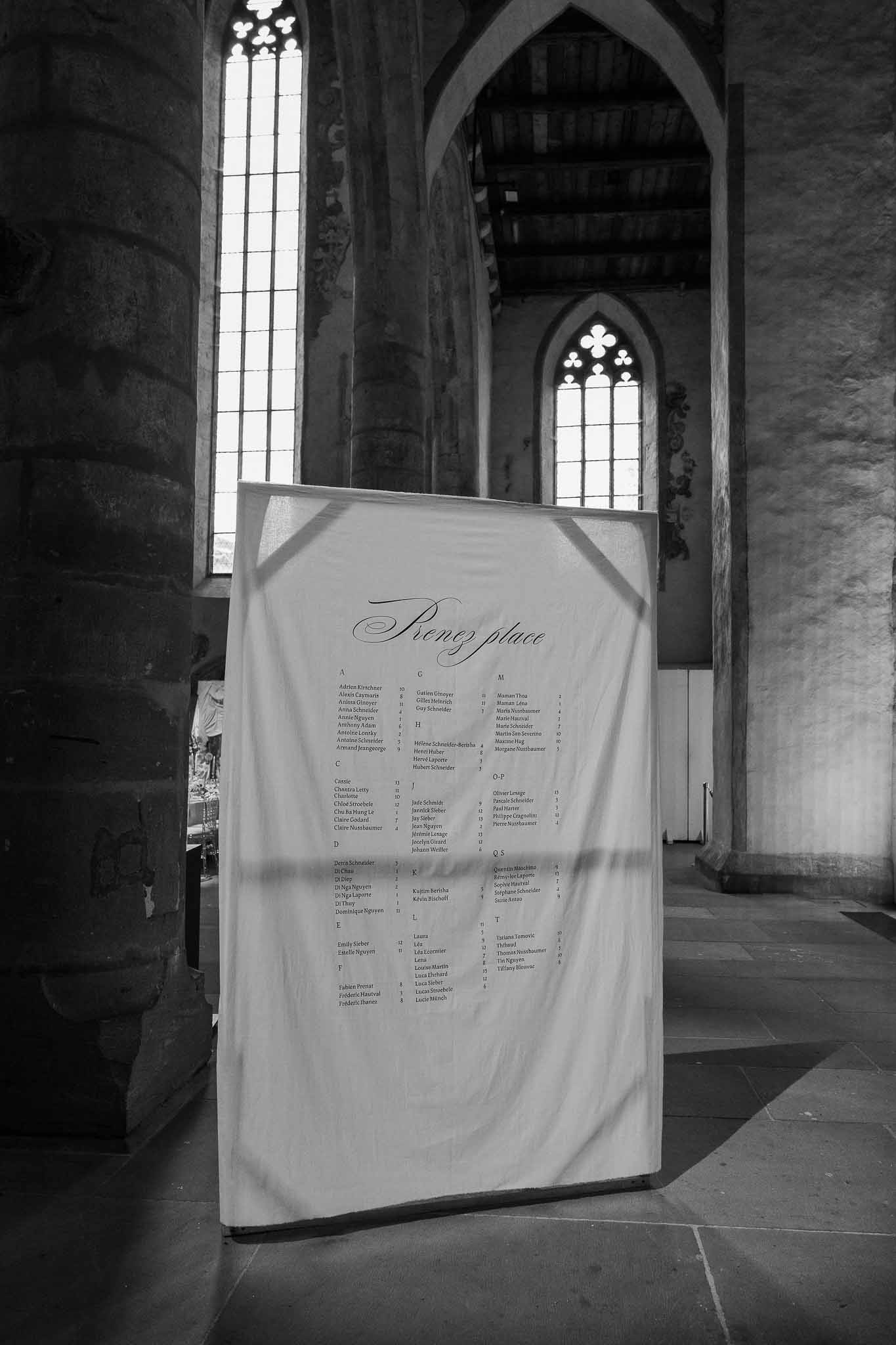 Black and white seating chart sign reading Prenez place in Gothic chapel with pointed arches and stone columns