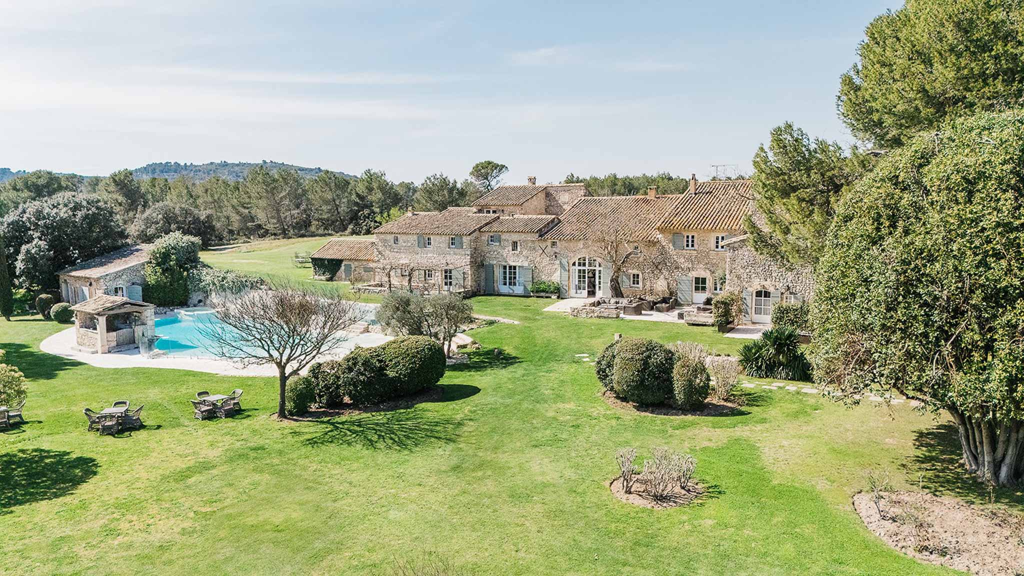 Aerial Provencal stone mas with terracotta roof turquoise pool trimmed hedges and blue-grey shutters on landscaped grounds