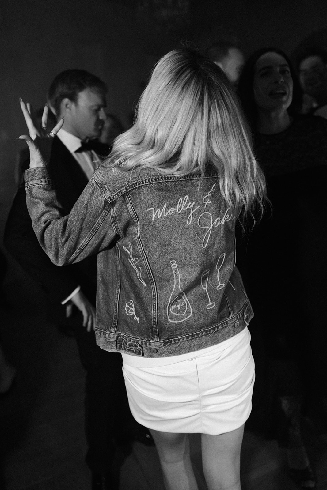 Black and white bride from behind wearing custom denim jacket reading Molly and Jake on dance floor