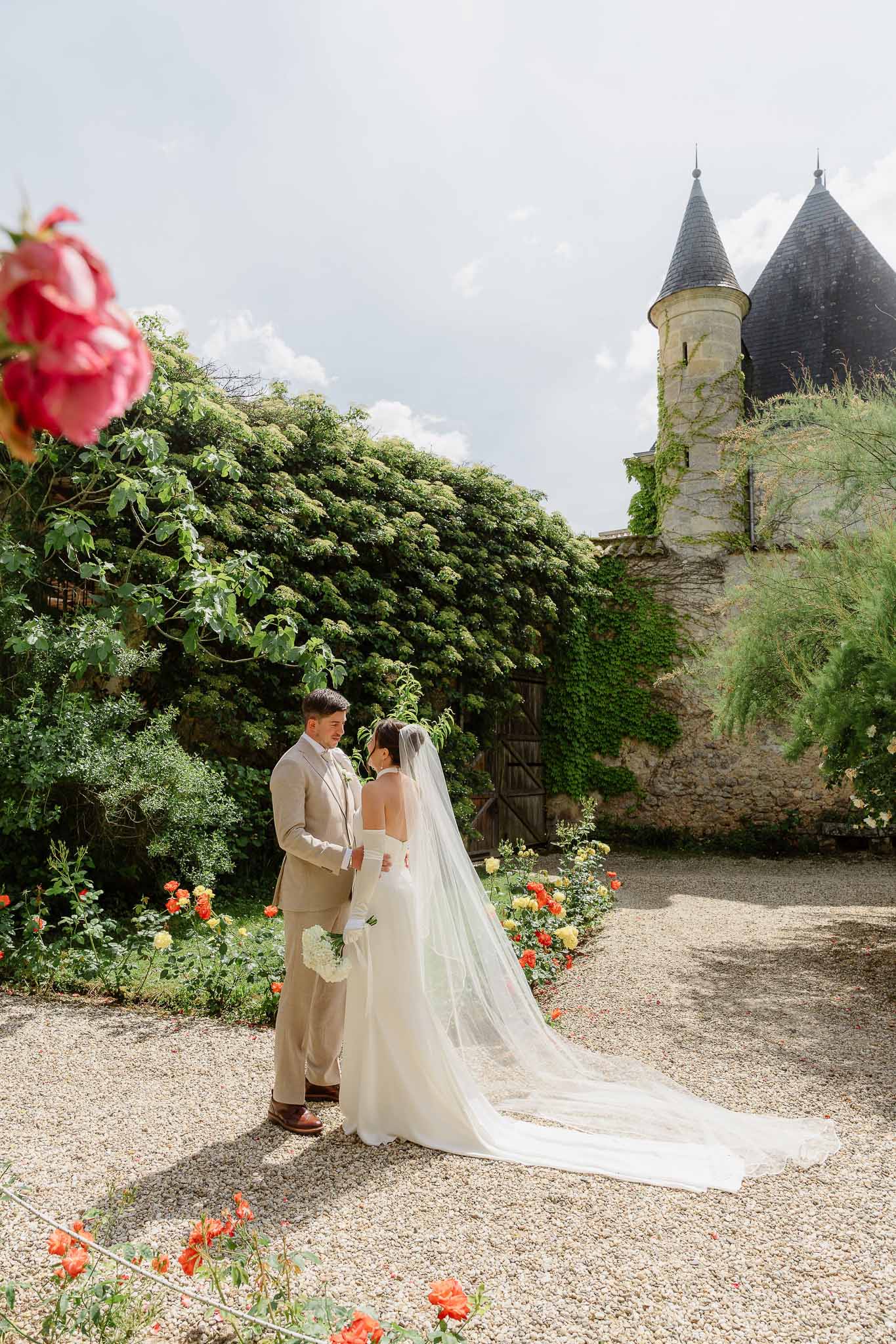 Couple facing each other at ivy-covered chateau turret, bride in gloves with cathedral veil on gravel