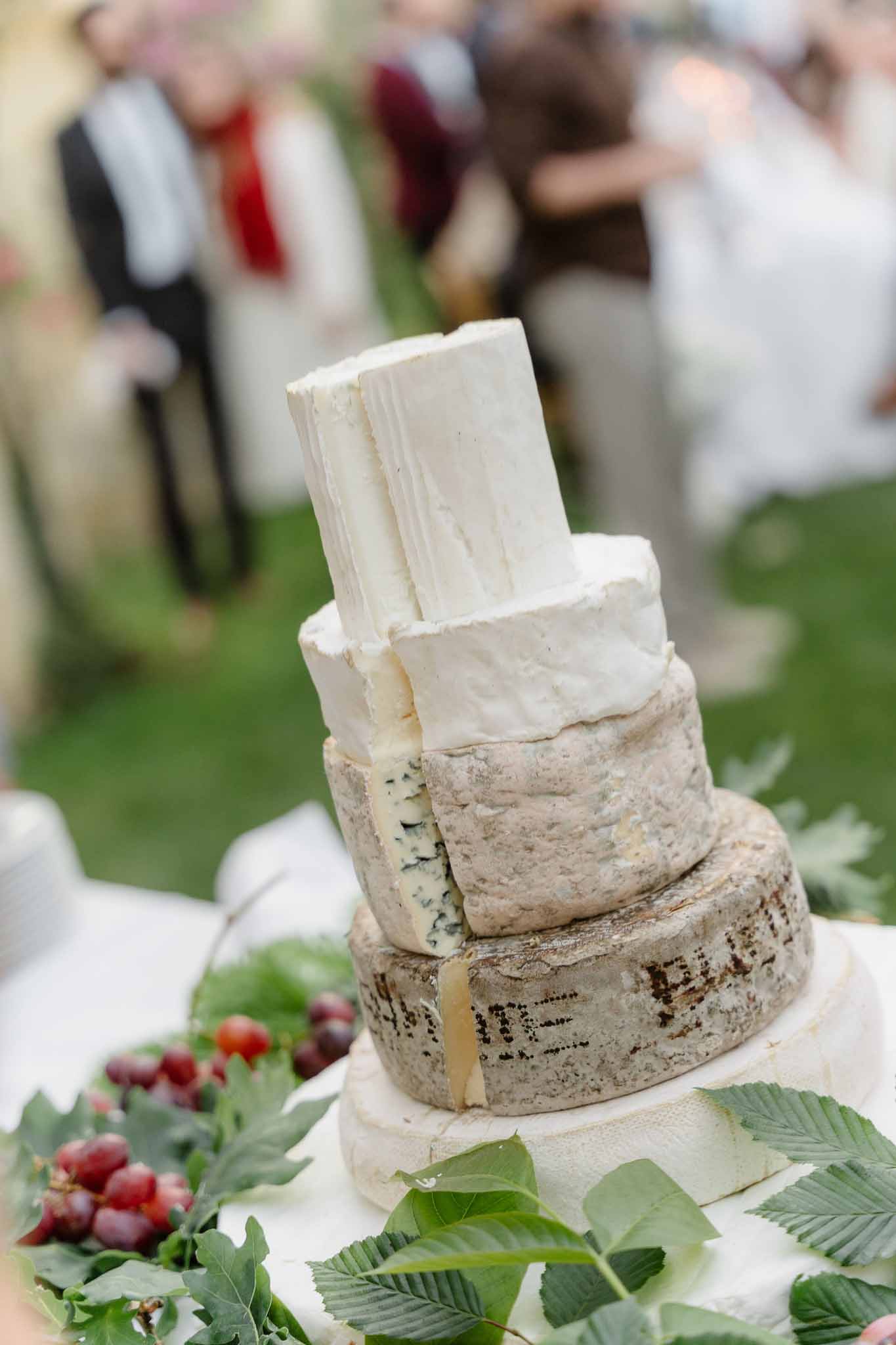 Four-tier French cheese tower with aged, blue-veined, and brie wheels styled with grapes and foliage