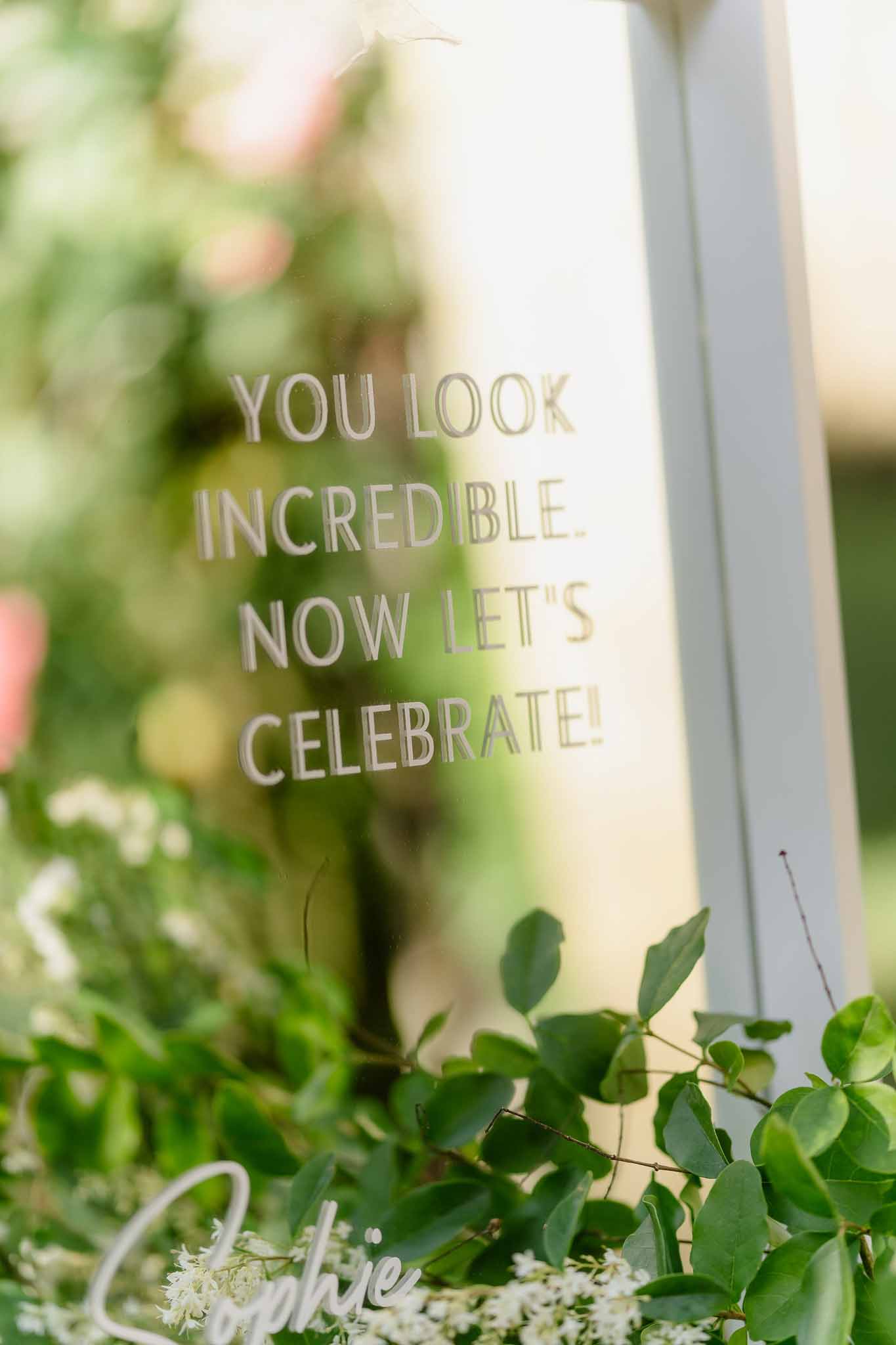 White-framed mirror welcome sign reading 'You look incredible' surrounded by green foliage in garden